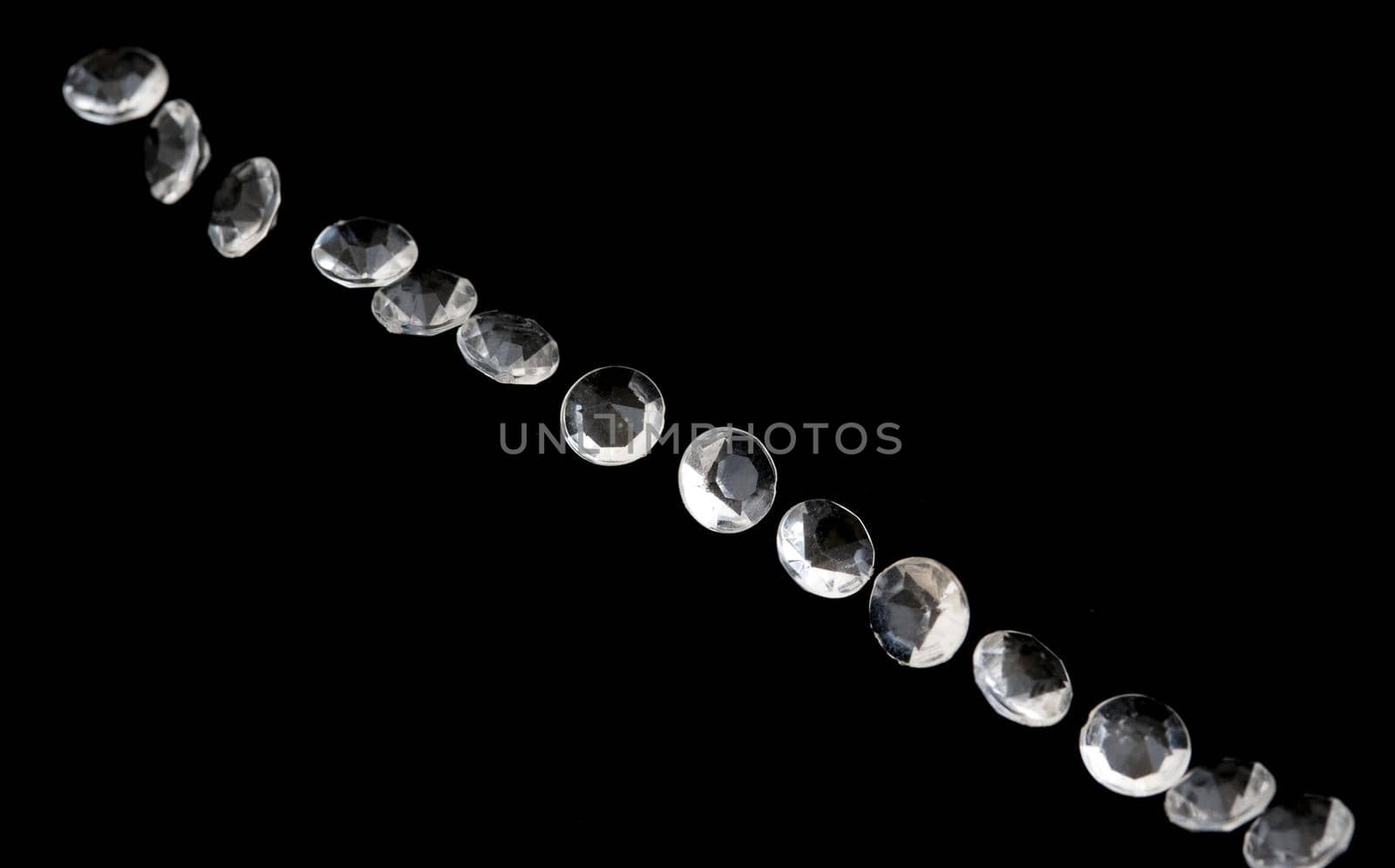 Diagonal line of faceted diamonds or gems sparkling against a black background with copy space on either side