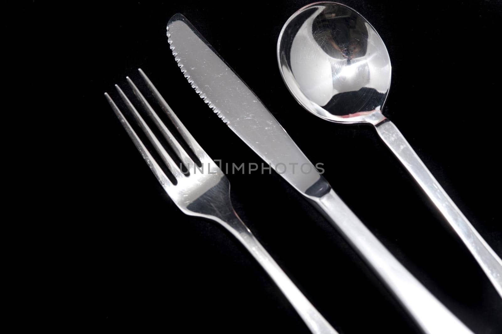Clean metal knife, fork and spoon on black background with copy space arranged diagonally from the left corner