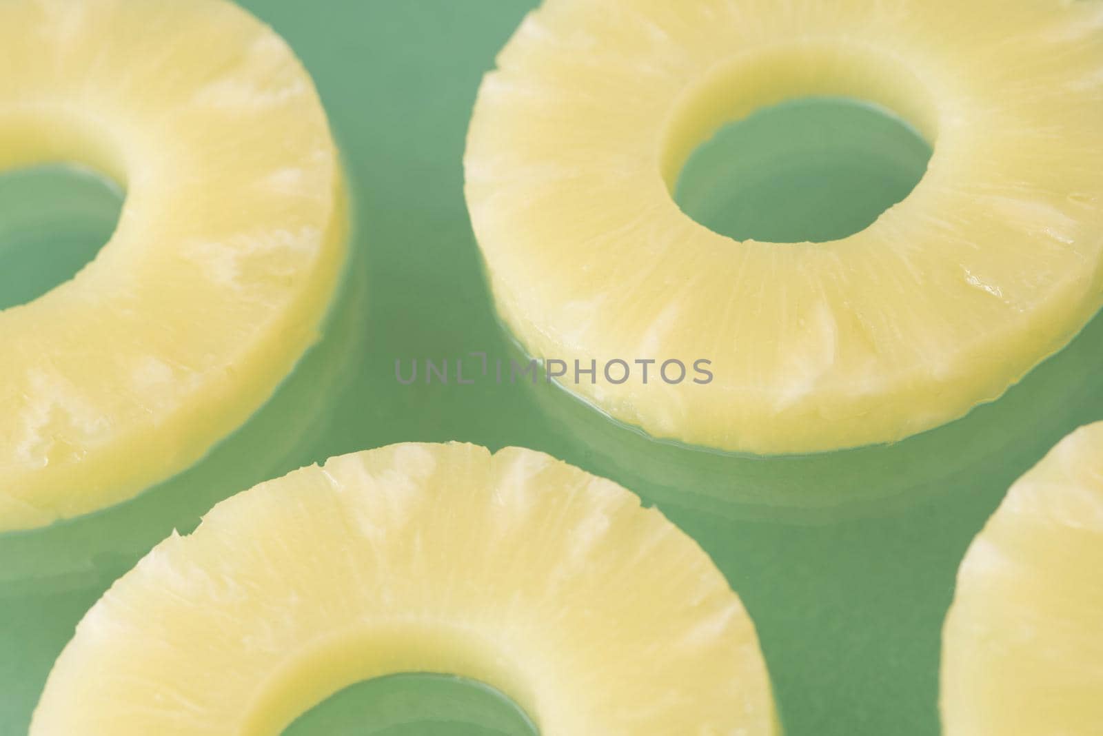 A close up of juicy, yellow sliced pineapple rings isolated on a plain green background with copy space.