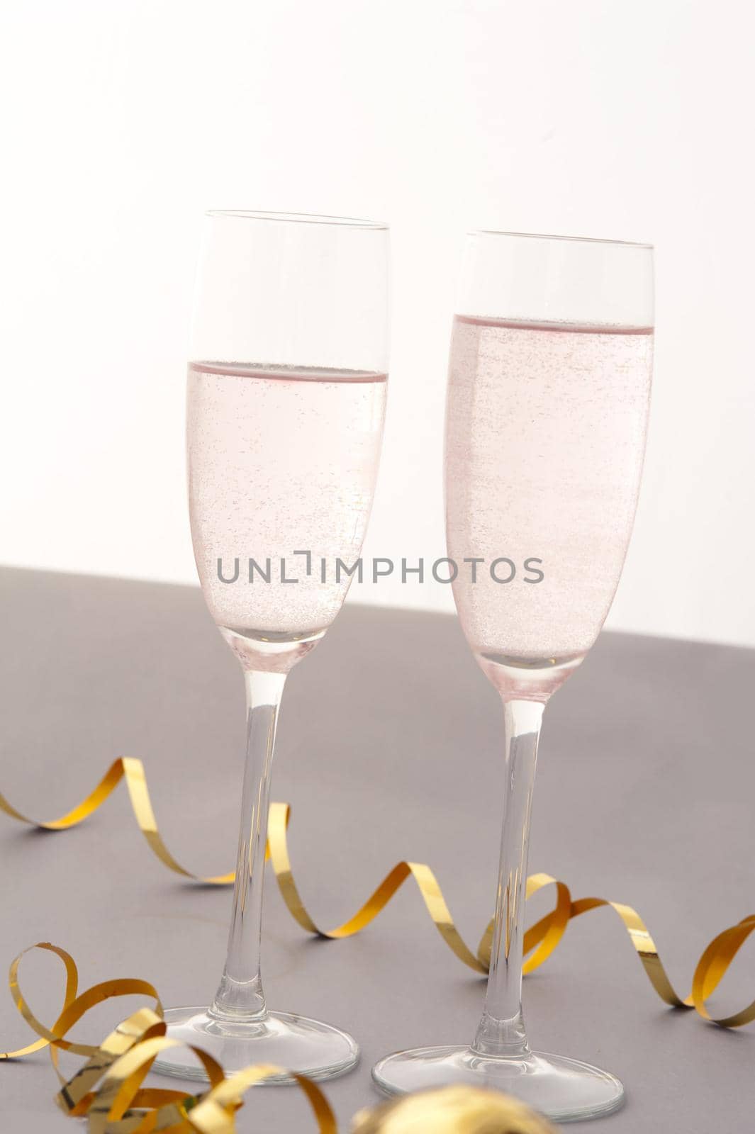Celebrating with two elegant flutes of sparkling pink champagne with twirled gold party streamers for a special romantic occasion