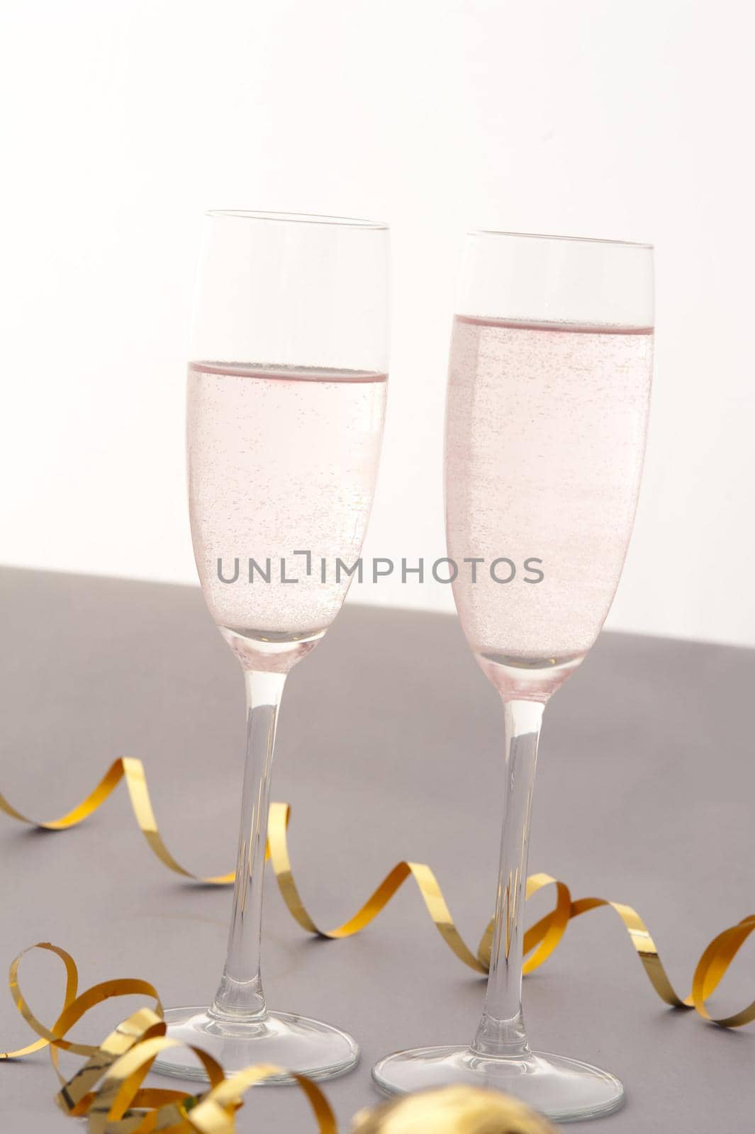 Celebrating with two elegant flutes of sparkling pink champagne with twirled gold party streamers for a special romantic occasion