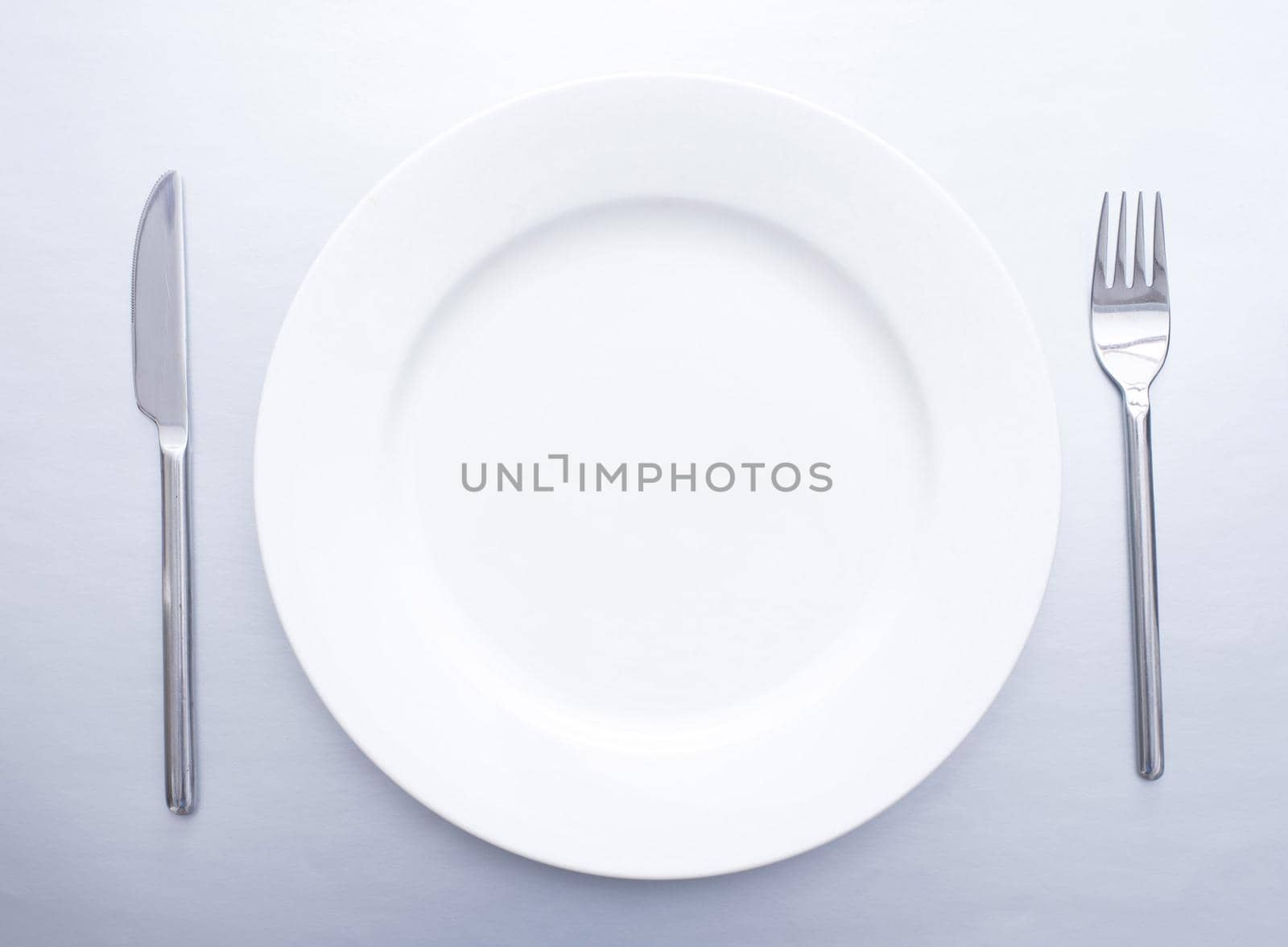 Plain simple place setting with empty white plate flanked by a silver knife and for viewed from overhead