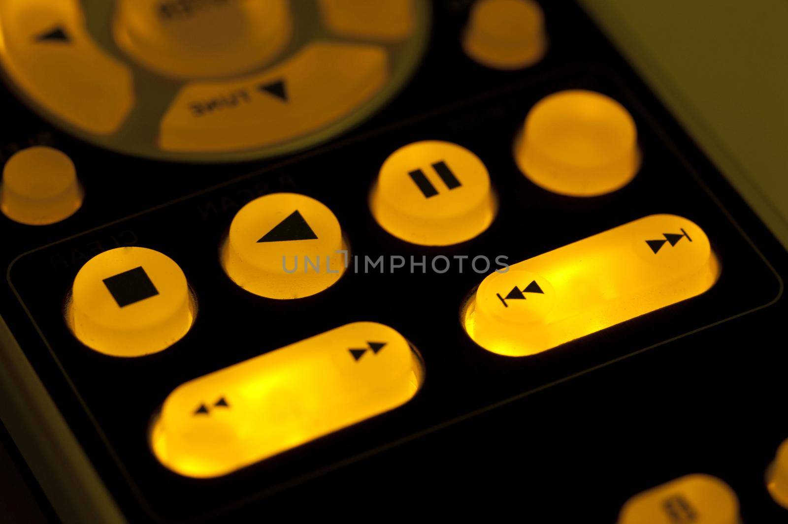Glowing remote control buttons in the dark, close-up on playback controls