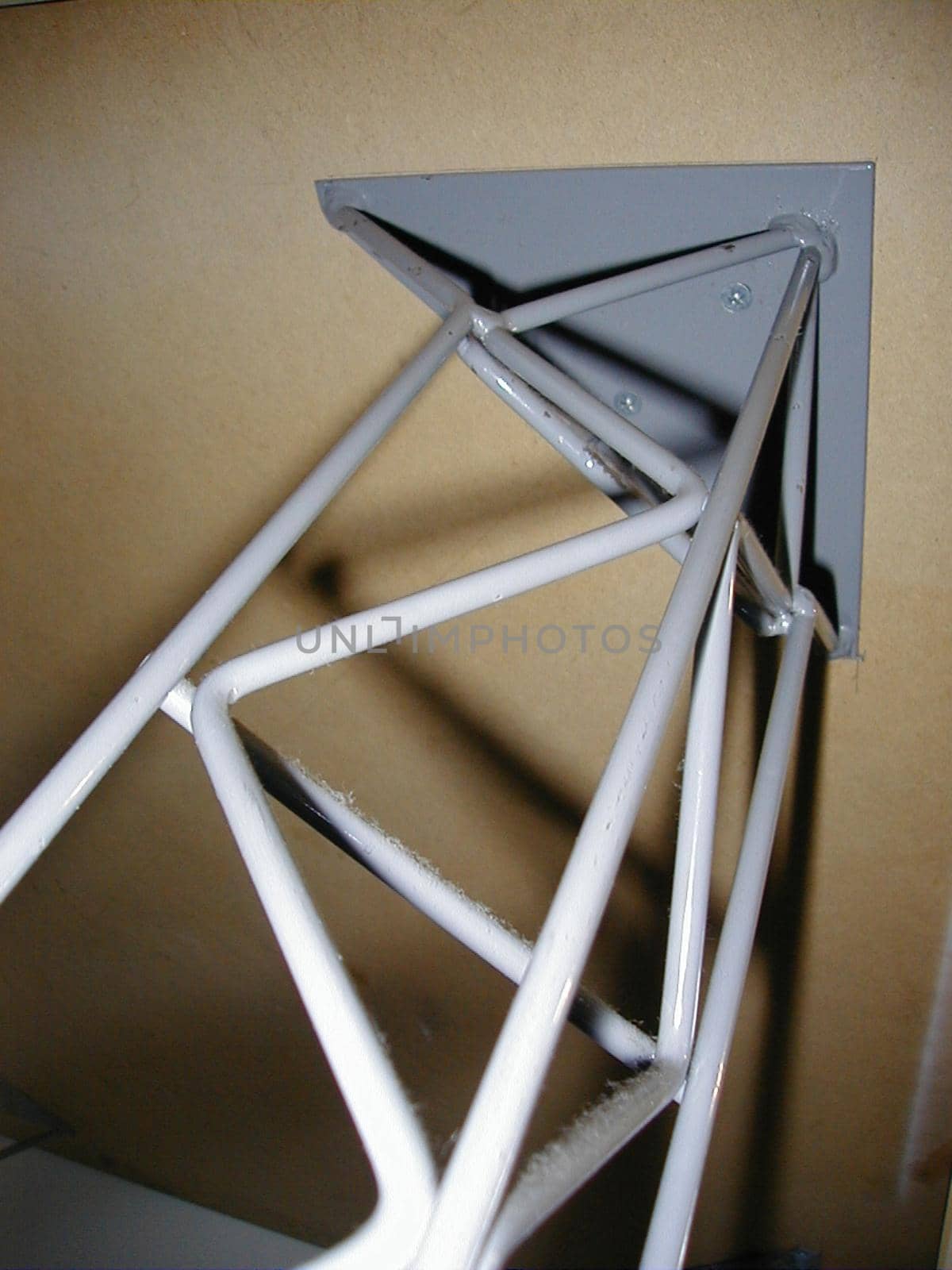 Metal truss of grey pipes welded to triangular iron element supporting wooden the sheet viewed in close-up and captured with flash light
