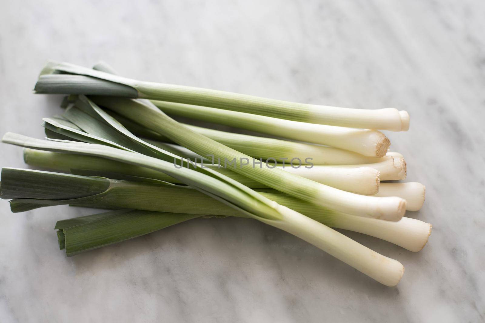 Bunch of fresh leeks in close-up on grey kitchen table surface. Cooking ingredients