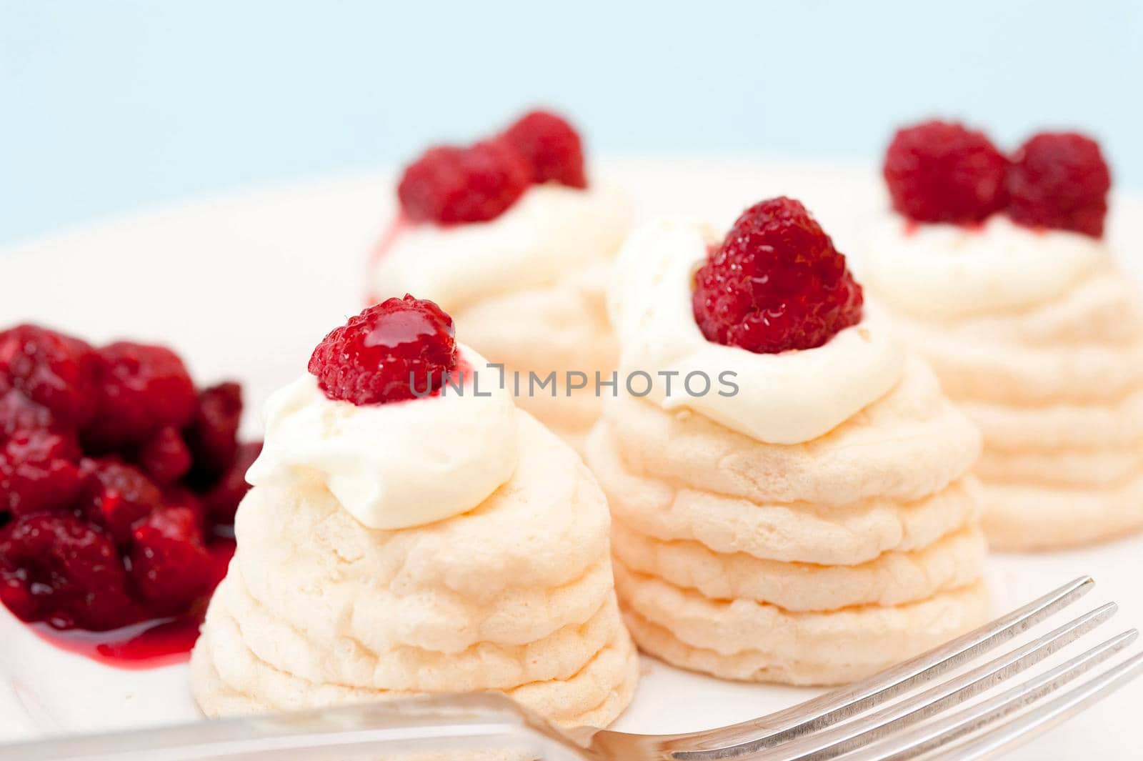 Individual twirled meringue cases filled with whipped cream and topped with fresh raspberry compote served on a plate