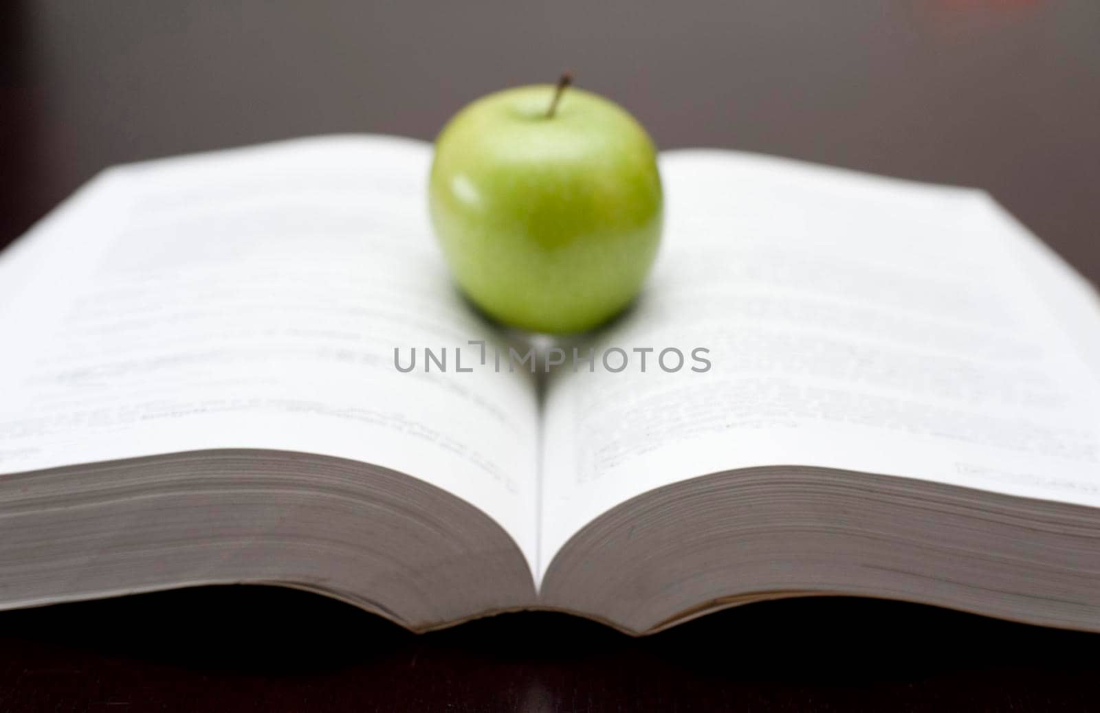 Fresh green apple balanced on the open pages of a textbook or novel in an education and learning or relaxation and reading concept
