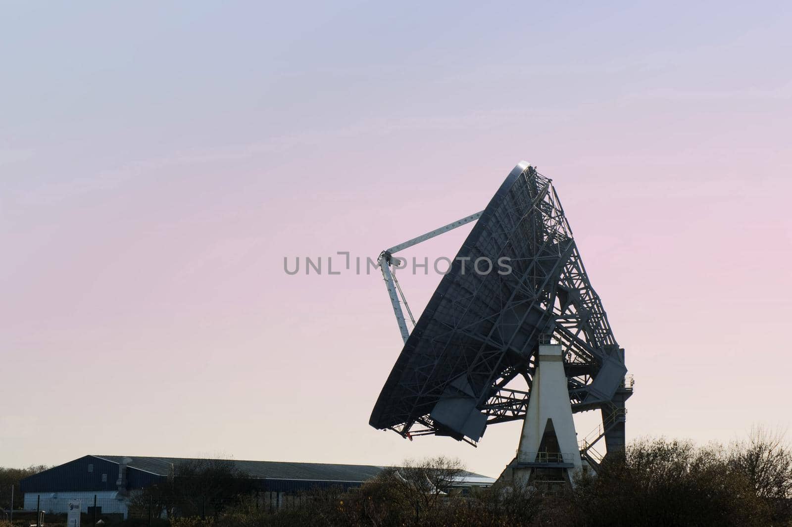 Silhouette of a satellite ground dish or parabolic antenna at sunrise or sunset against a colorful pink sky with copy space in a communications concept