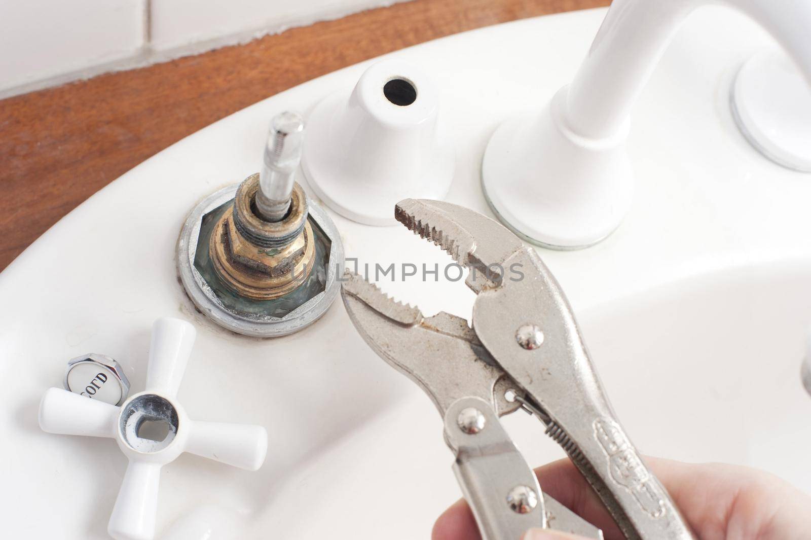 Man doing home plumbing maintenance fixing a faucet or tap on a sink with a mole grip wrench