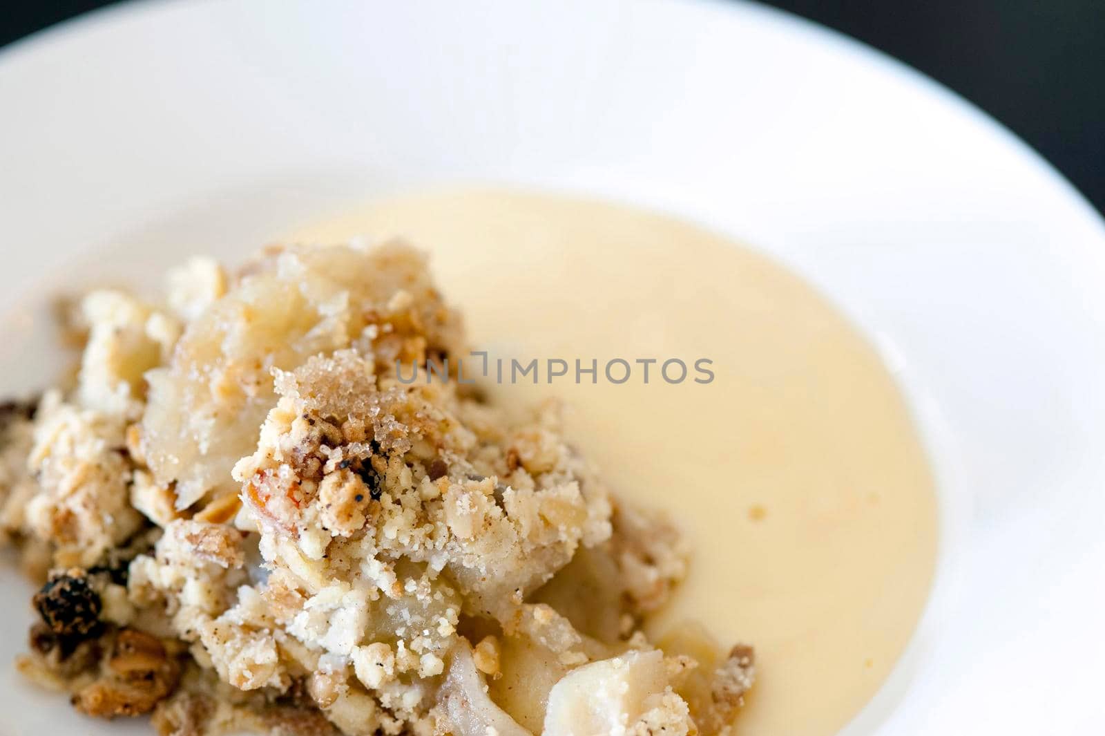 Plate of delicious baked apple crumble and custard with a spicy topping using cinnamon and raisins, closeup view