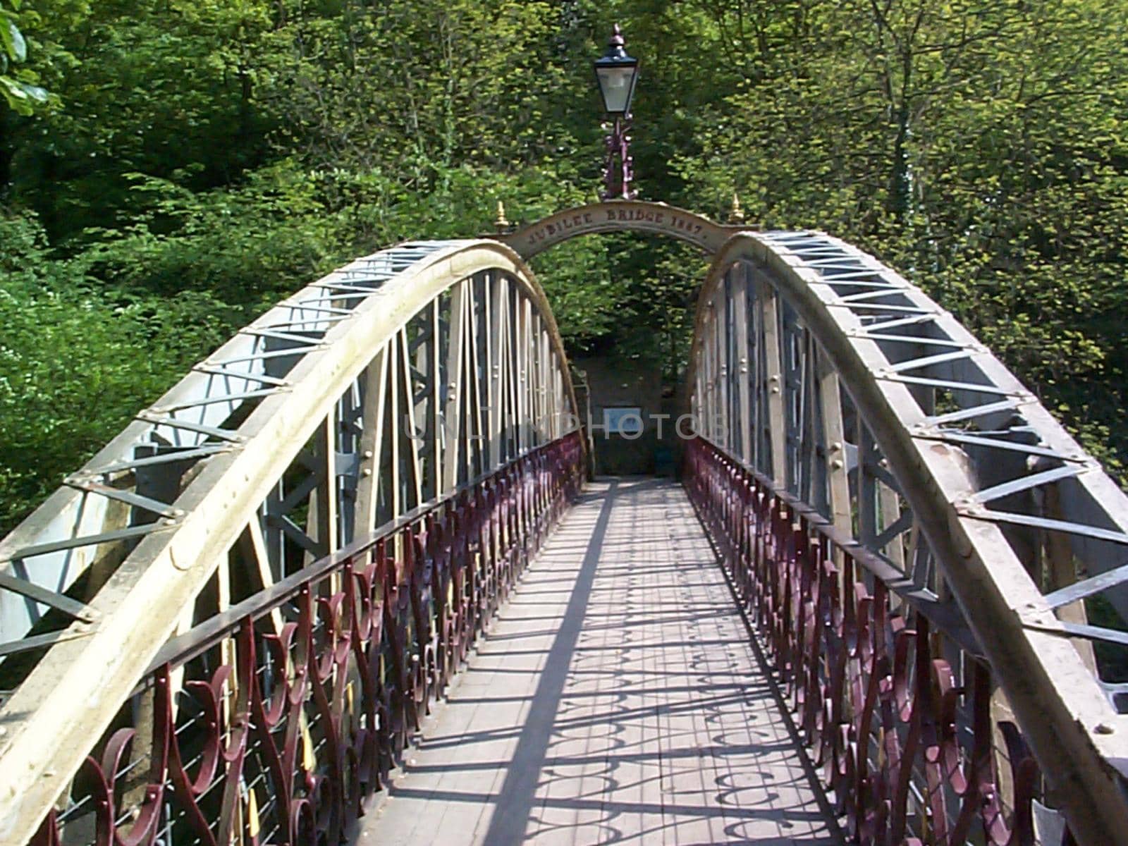 Pedestrian walkway across an arched steel bridge in a receding view leading to leafy green trees