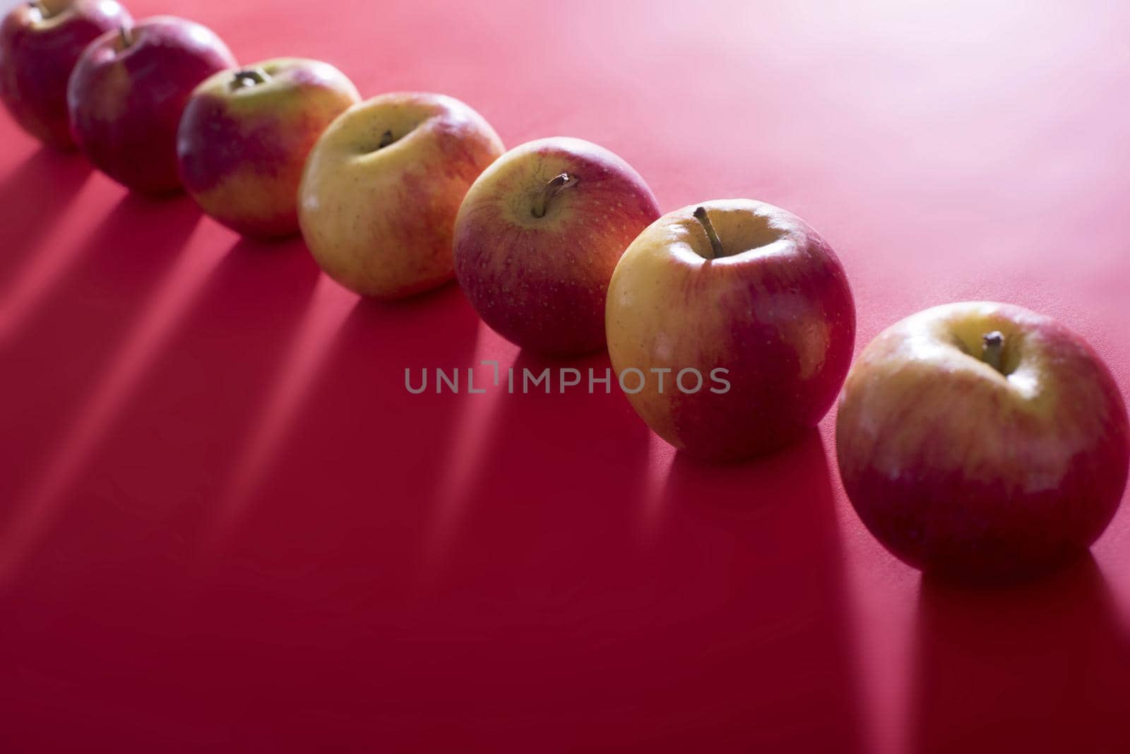 Diagonal line of fresh whole apples backlit on a festive red background casting a shadow over copy space