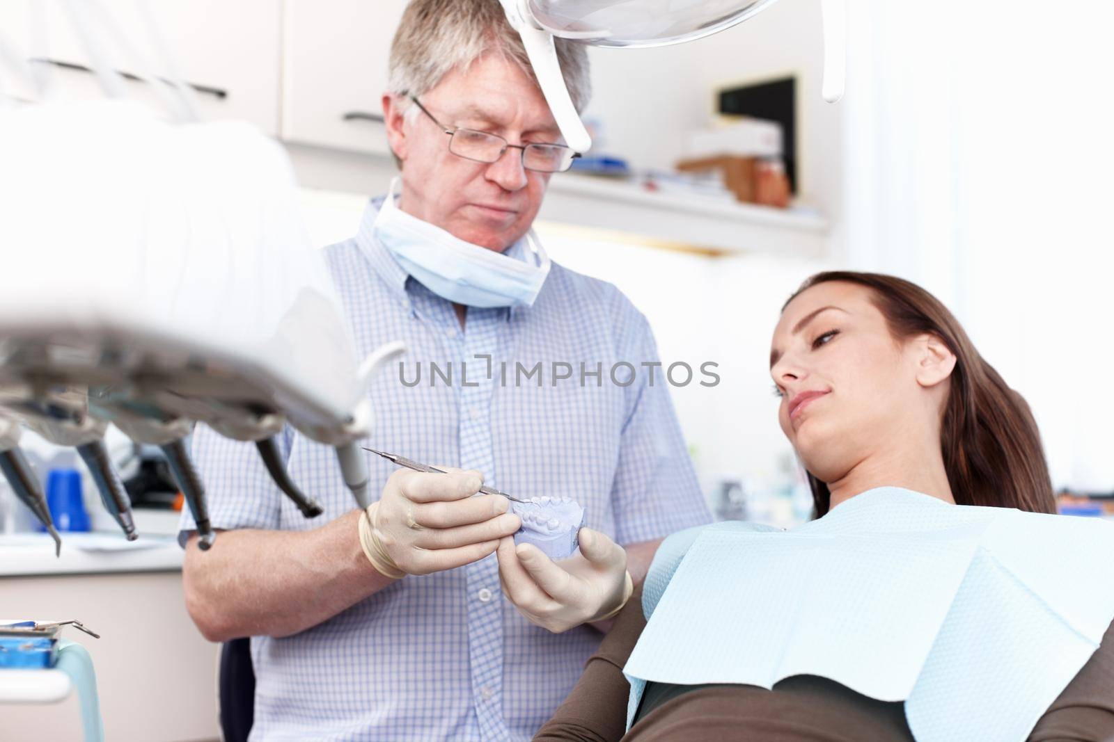 Dentist holding false teeth in clinic. Portrait of dentist holding false teeth with female patient in clinic