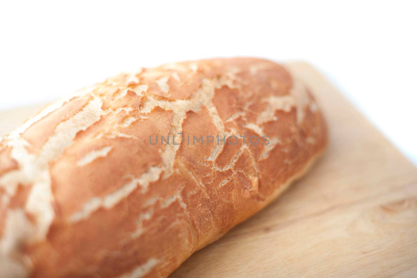 Close up view with shallow dof of a freshly baked crusty loaf of white bread on a wooden bread board over white