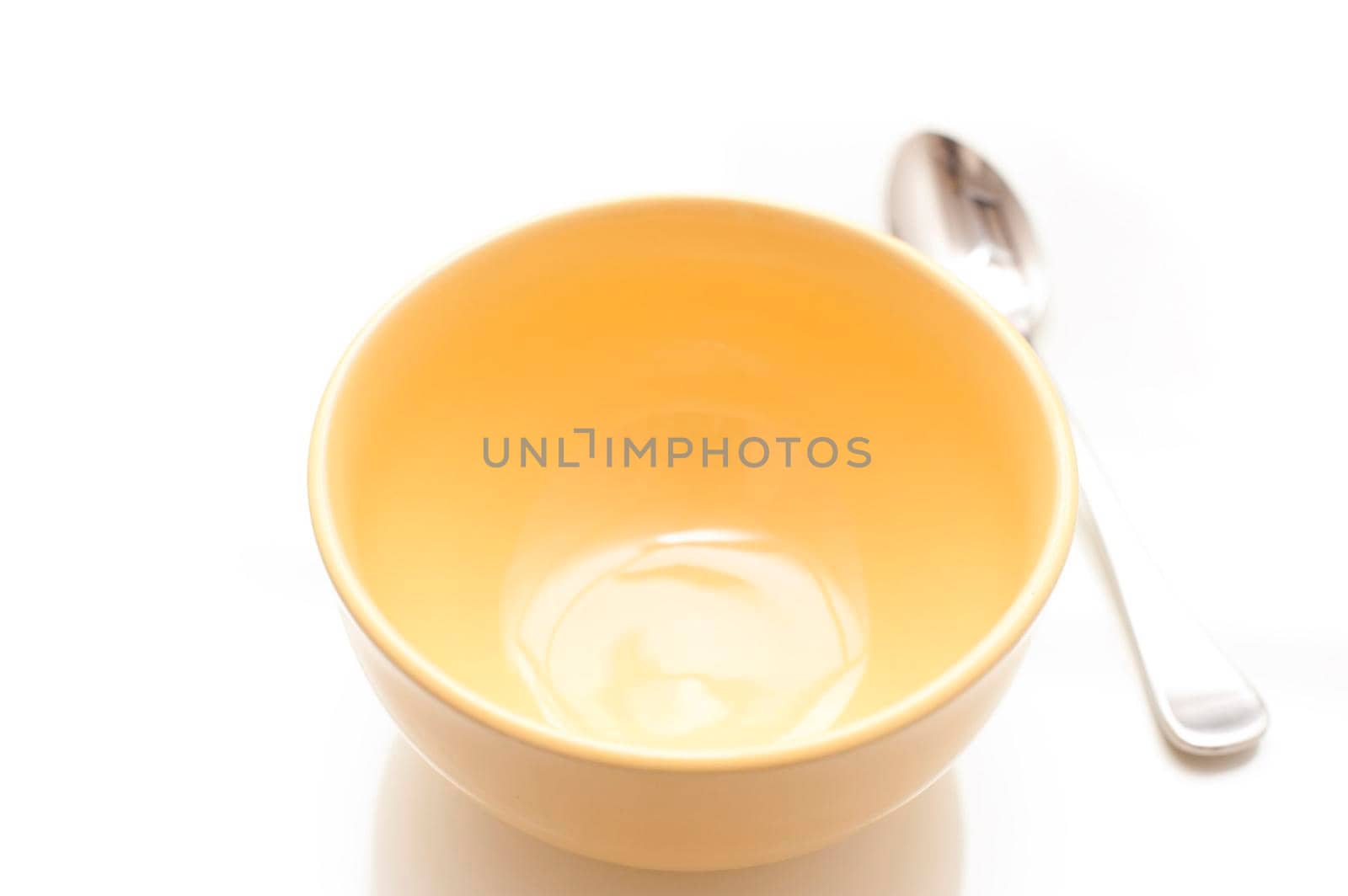 High angle close up view of an empty yellow ceramic breakfast bowl and spoon on a white background