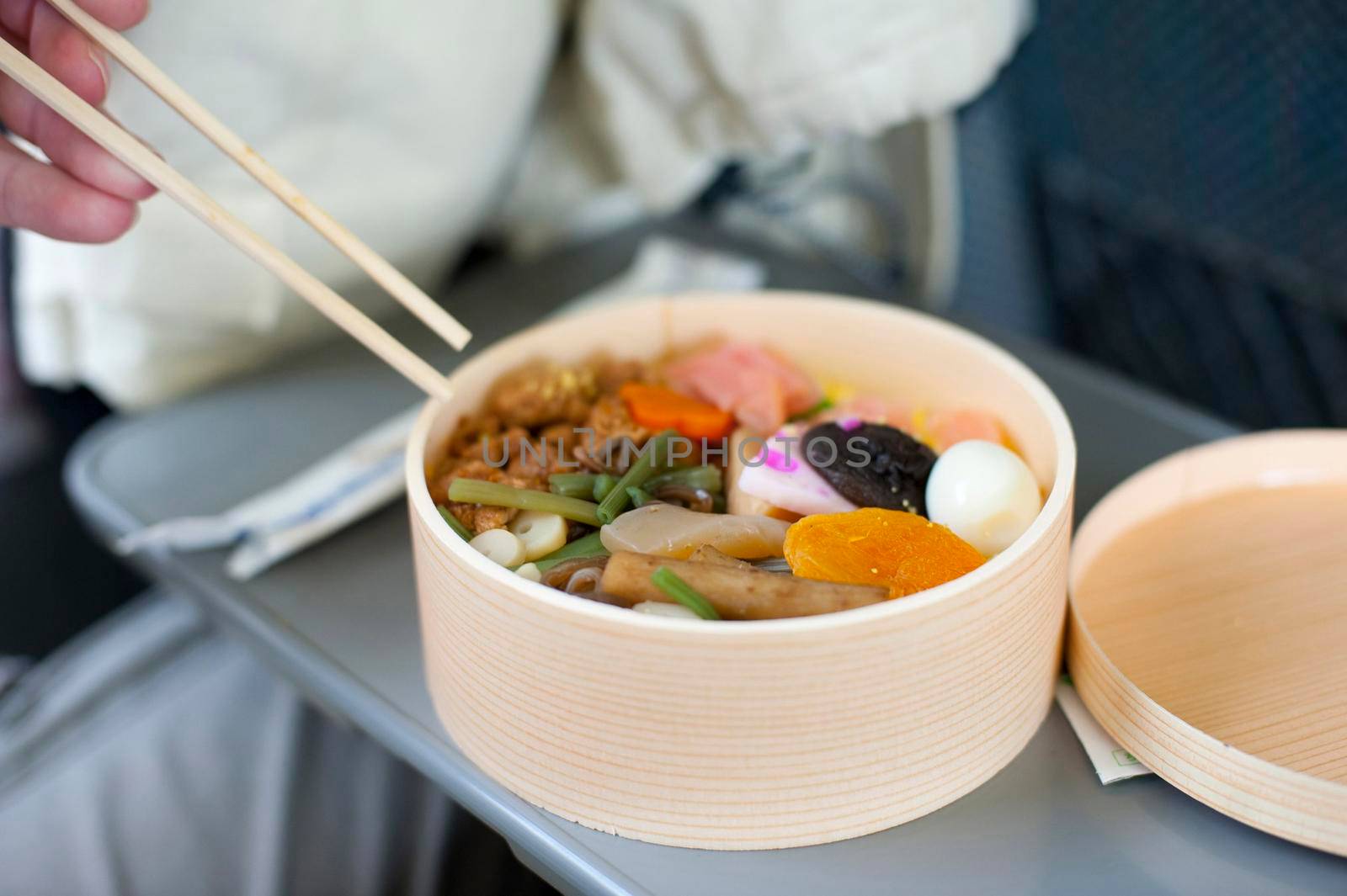 Bento, or obento, box with Japanese food, a traditional lacquered container for serving a whole meal particularly lunch, mans hand holding chopsticks