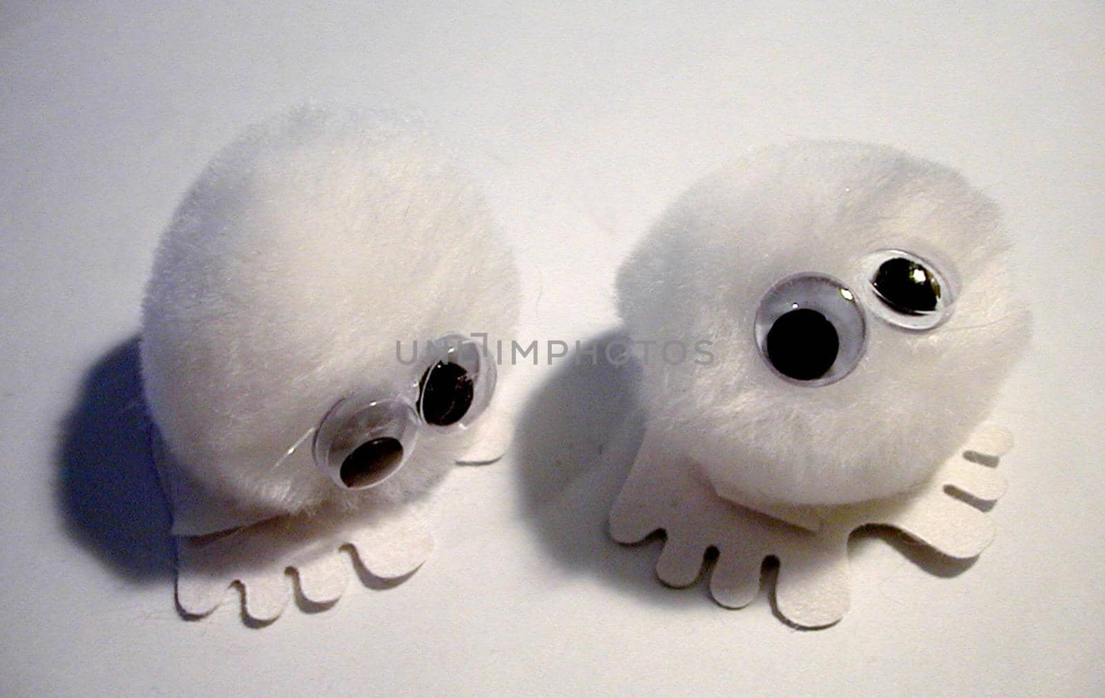 Overhead view of cute fluffy white puff balls with felt feet and glued on eyes