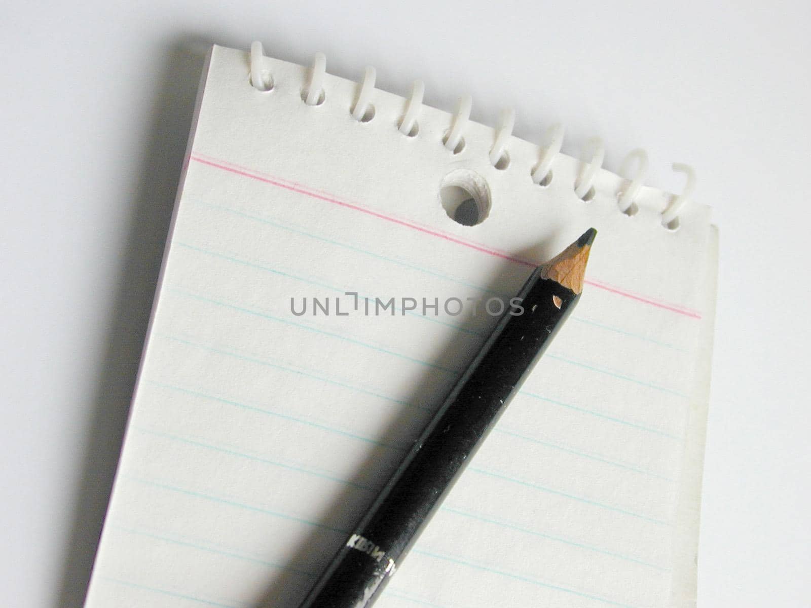 Close up view of short black pencil placed on a blank lined notepad against a white background