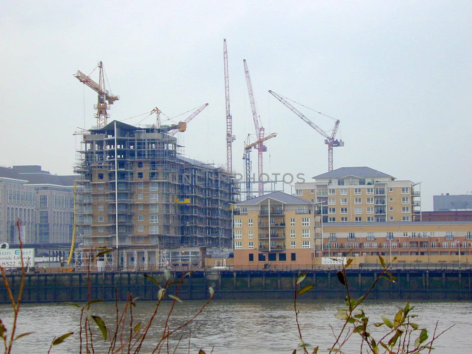 Waterfront urban construction of high-rise buildings surrounded by lots of industrial cranes viewed over the water on a misty day