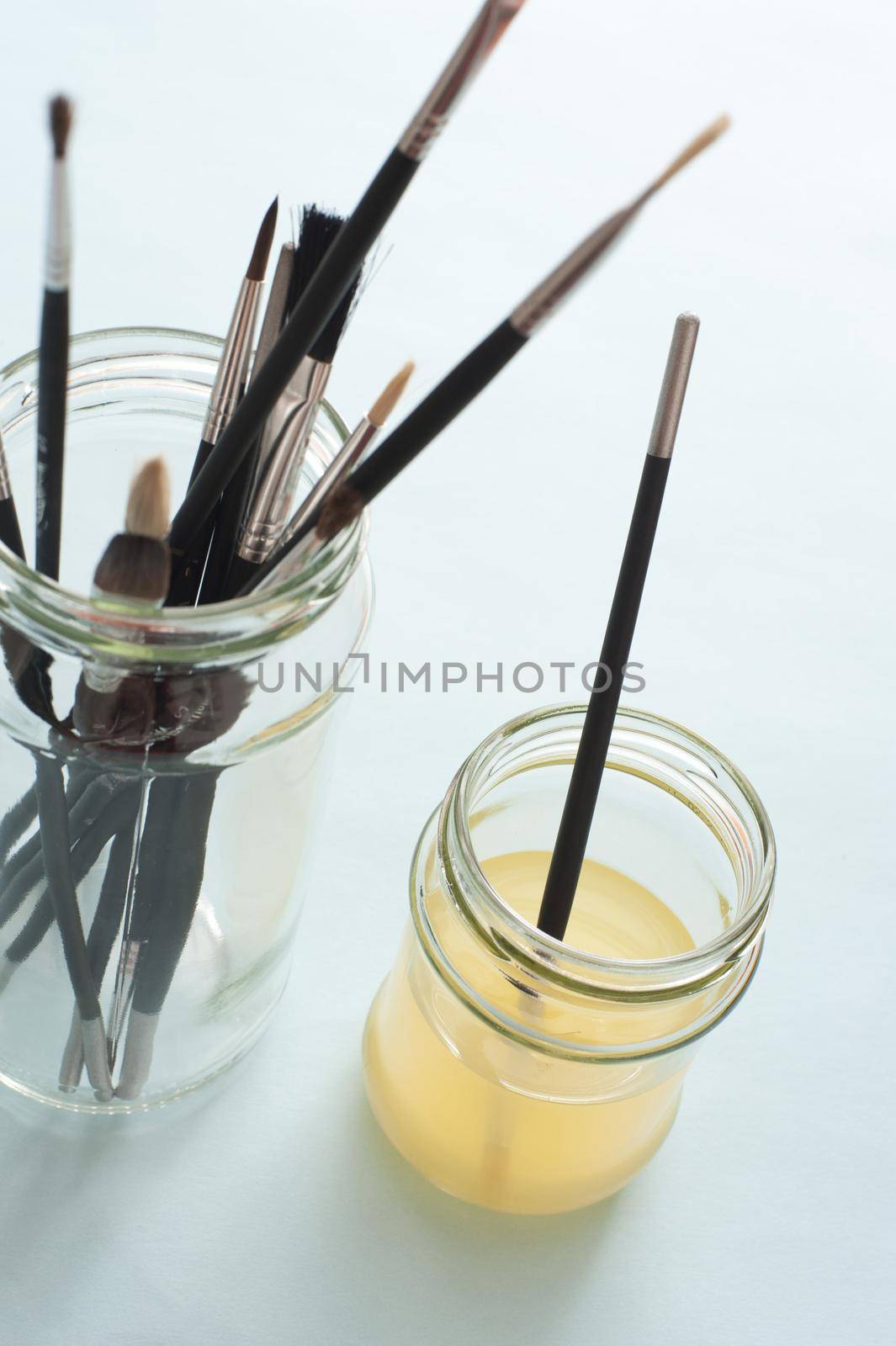 Single brush in cloudy water wash next to taller jar of various dry paintbrushes