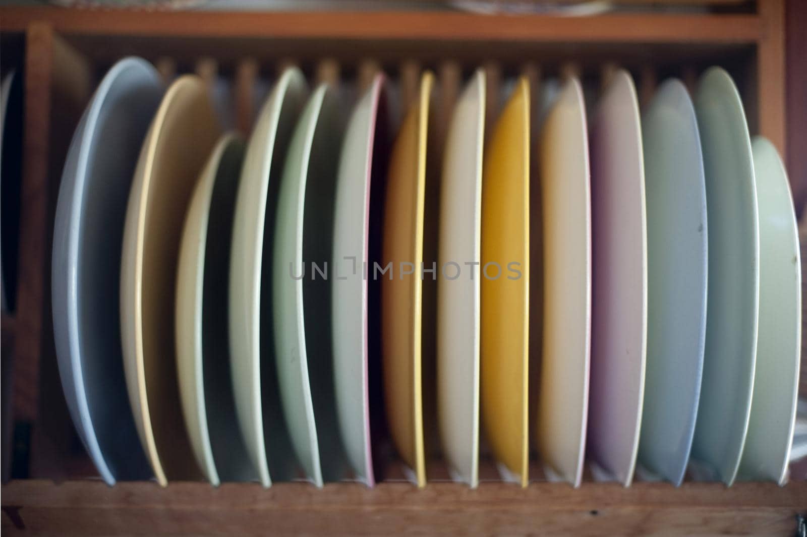 Selection of clean colourful dinner plates in a wooden rack mounted on a kitchen wall ready to be used to serve the food