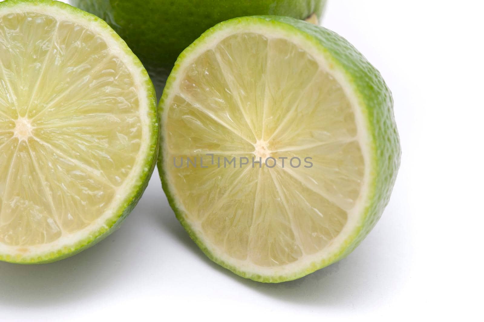 Closeup of a halved fresh lime showing the pulp texture and segments on a white background