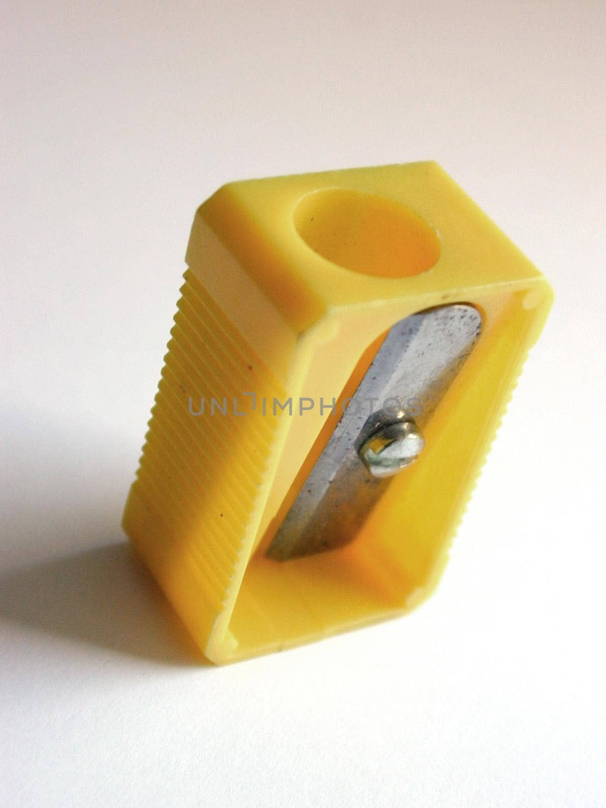 Yellow plastic pencil sharpener standing upright on white with the blade towards the camera