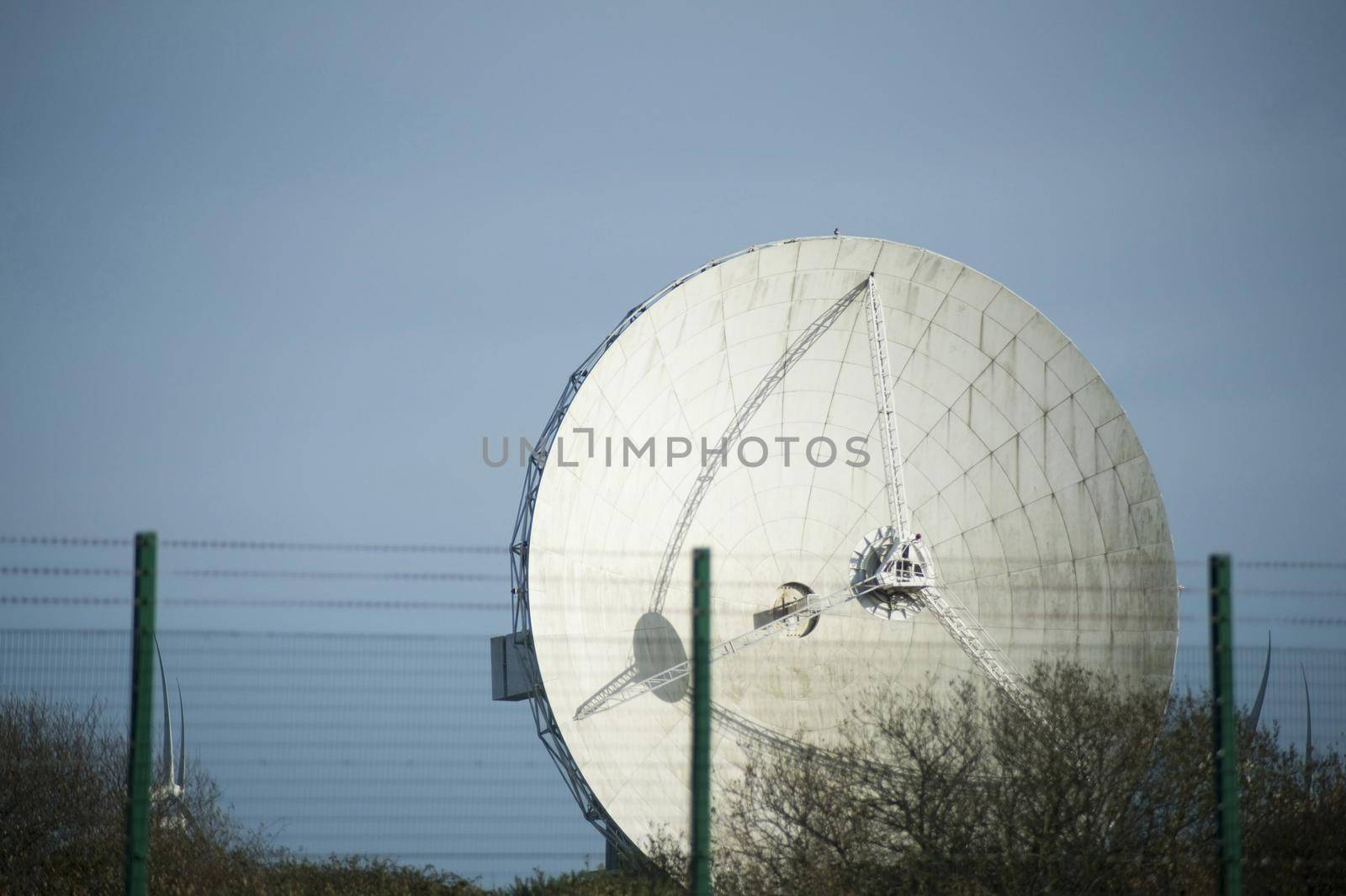 High barbed wire security fence in front of a parabolic satellite antennae installation on the skyline in a concept of security