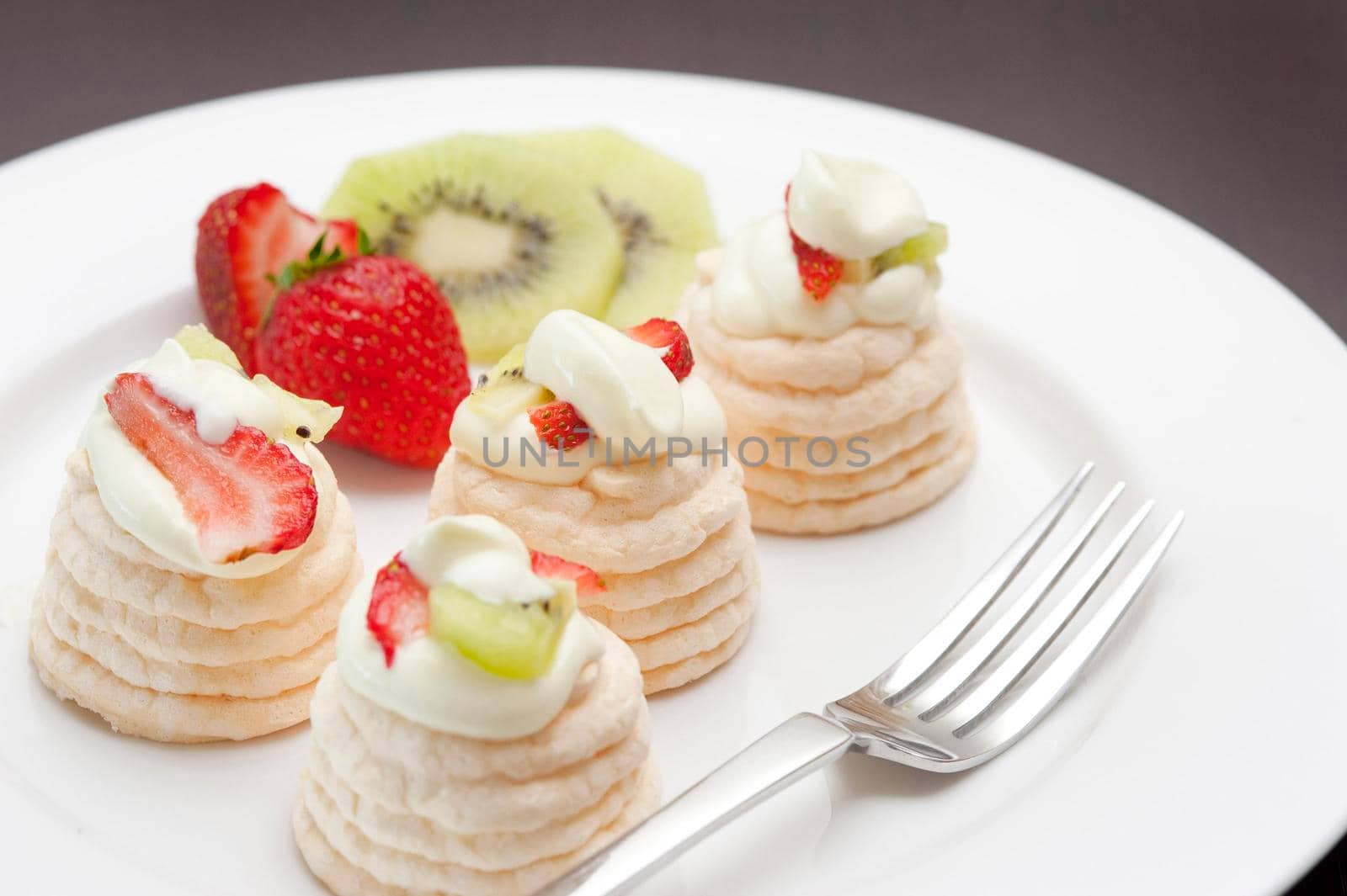 Meringue dessert with small individual meringues filled with cream and topped with kiwi fruit and strawberries