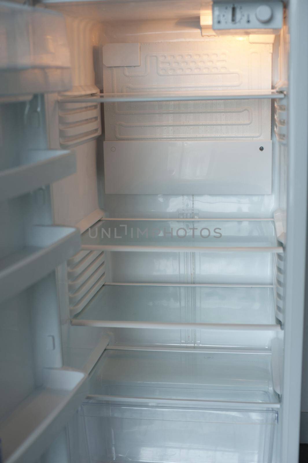 Open empty white refrigerator interior with shelves and compartments illuminated by the interior light showing it is on and connected to electricity