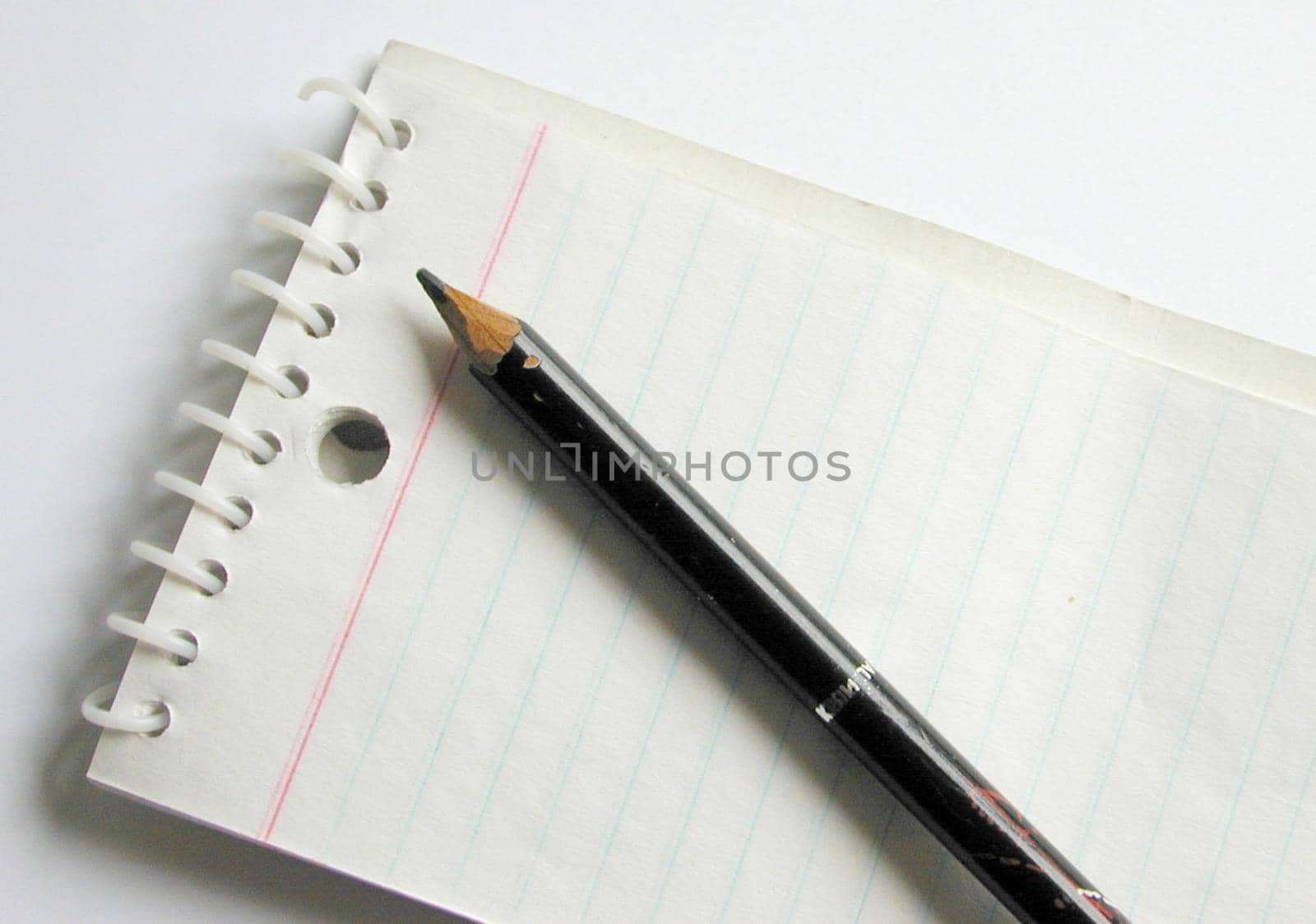 Pencil lying on a blank ruled spiral bound notepad viewed diagonally from above in a business or school concept