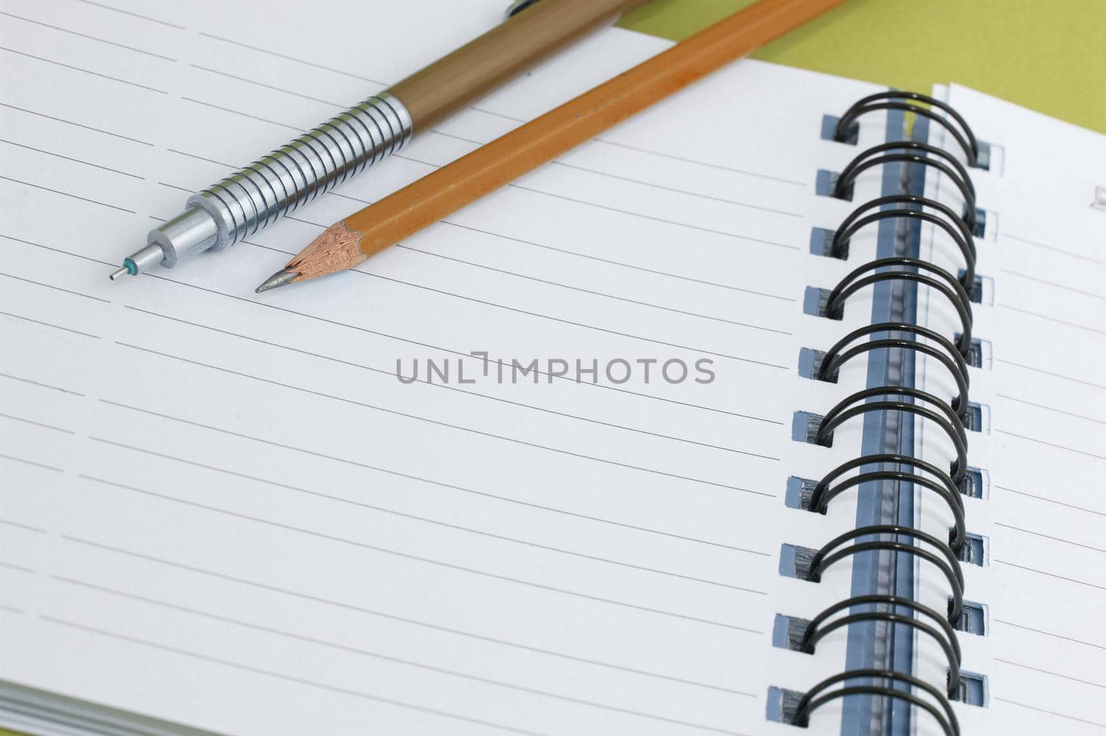 A mechanical and a sharpened wooden pencil lying on a blank lined page of a notebook