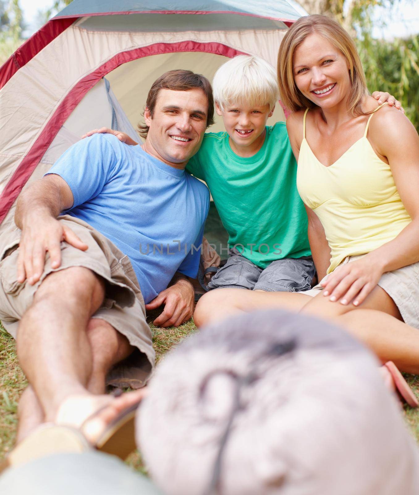 Attractive family camping. Portrait of an attractive family of three sitting in front of tent and smiling