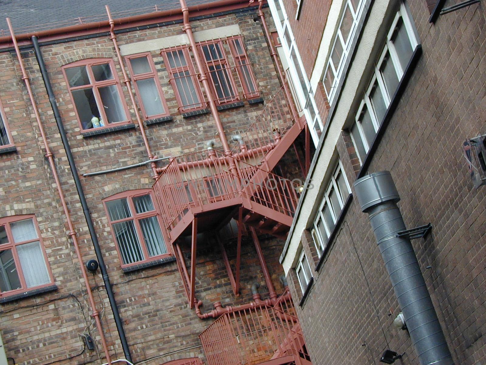 Red metal fire escape on the exterior of a an old face brick building viewed at a tilted angle from below