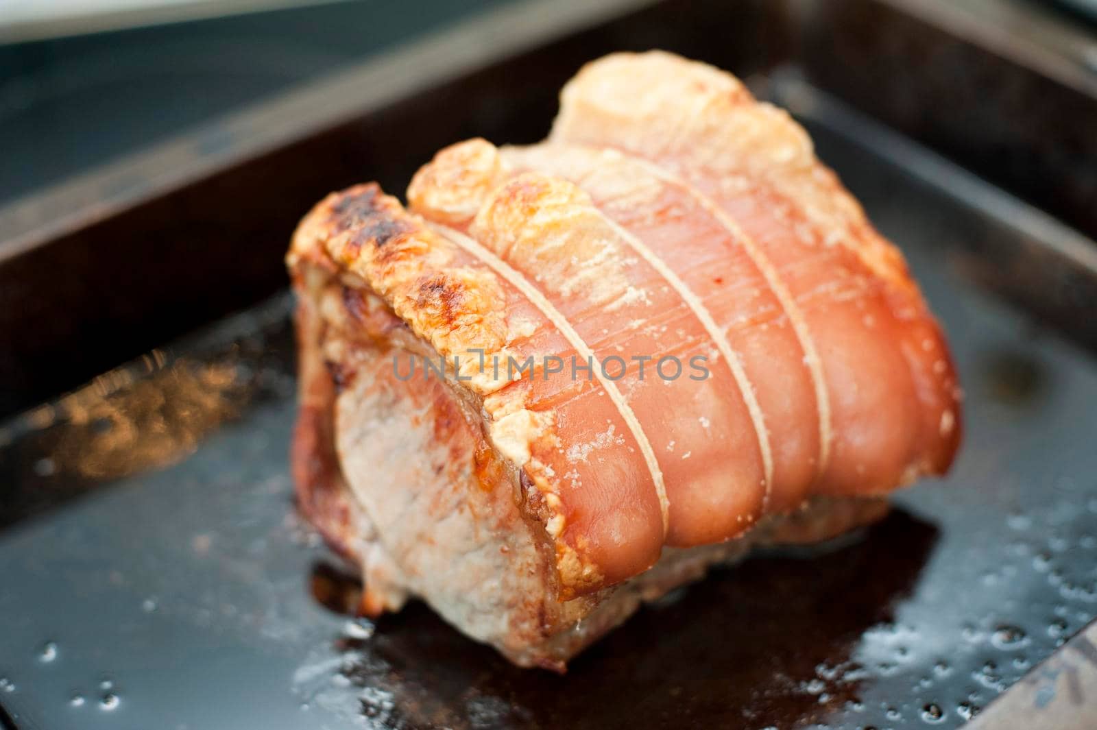 Crispy crackling on a cut of rolled roast pork in a grill pan, closeup view of the meat and the golden texture of the crackling