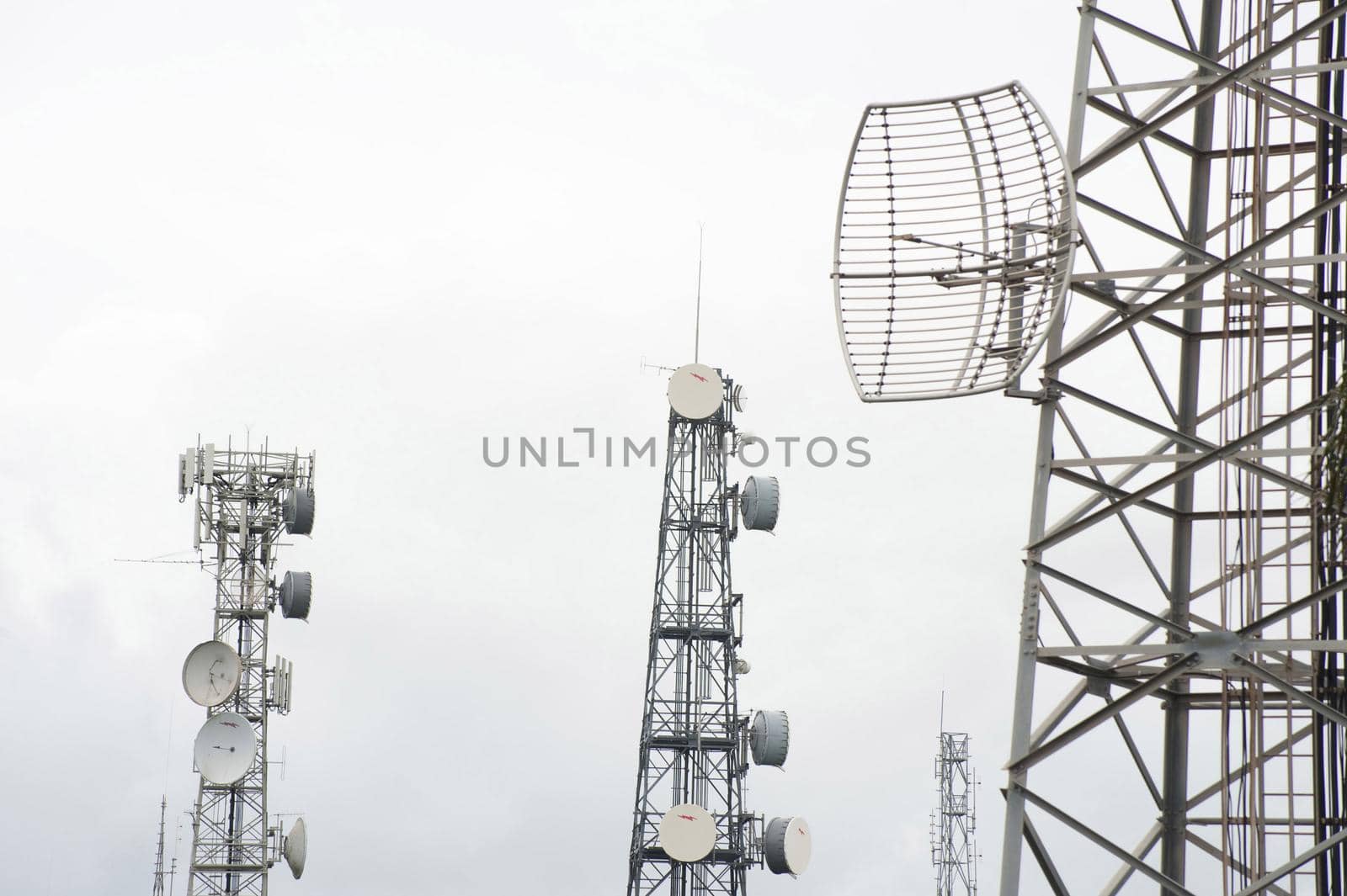 Three mobile telecommunications towers in mist or cloud with dish antennae to receive and transmit radio signals
