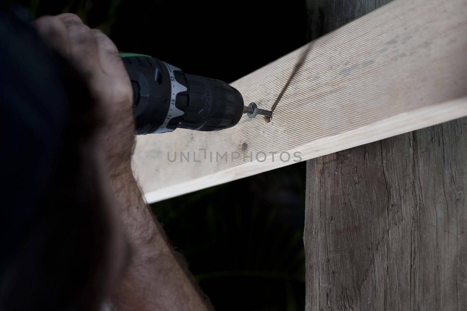 Man fixing wood to a support with a screw using a screwdriver attachment on his electric drill, close up of his hand and the drill bit