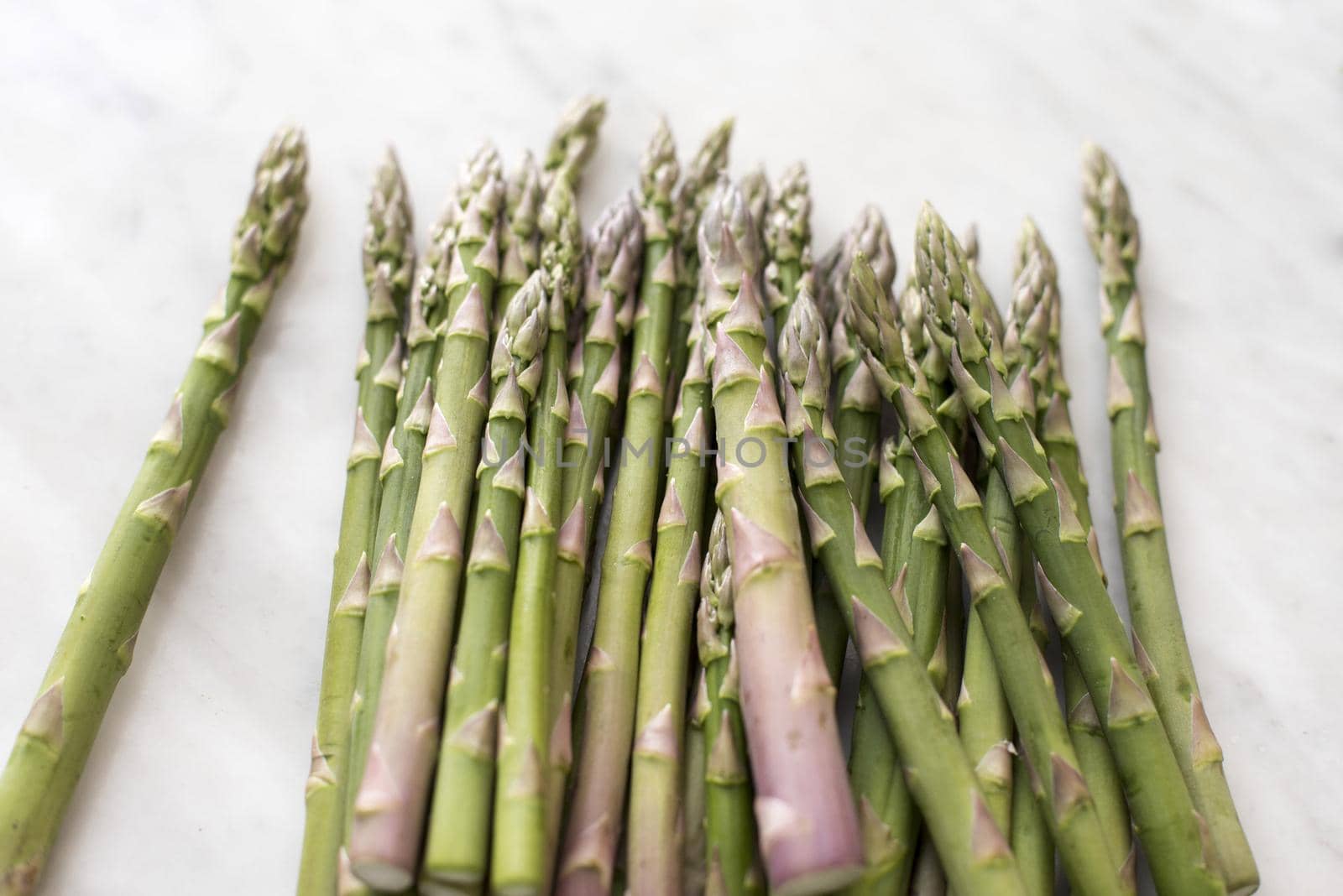 Pile of fresh raw seasonal green spring asparagus tips, shoots or spears on a white background