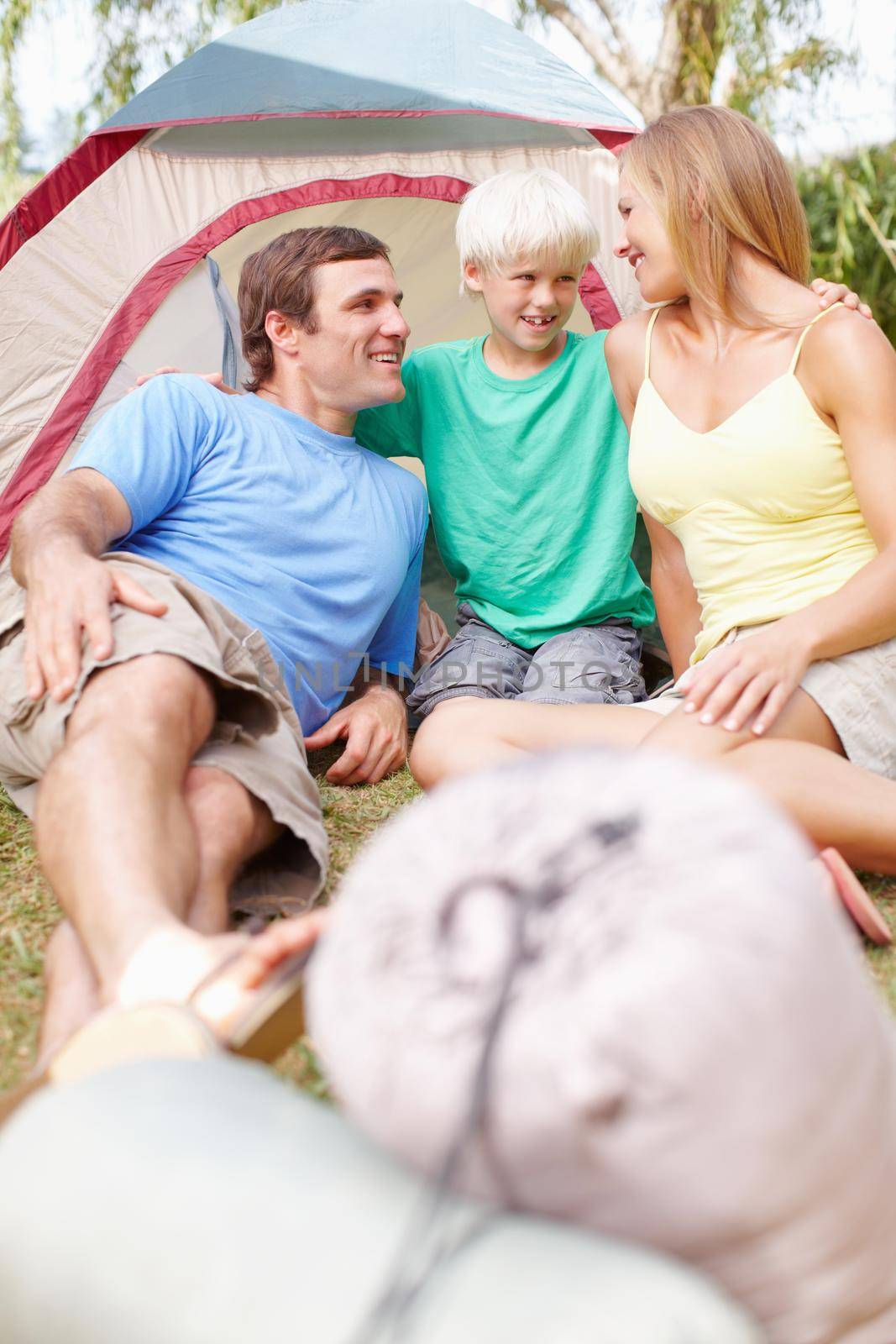 Happy family camping. Happy family of three relaxing in front of tent and looking at each other. by YuriArcurs