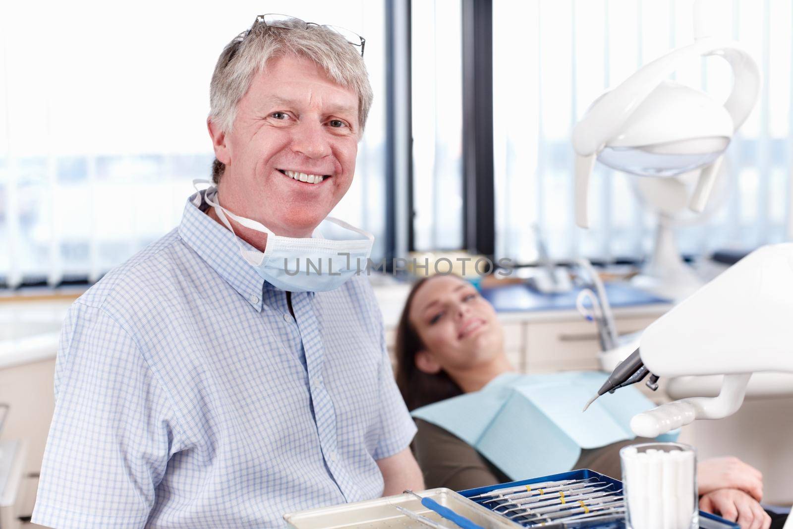 Happy dentist with patient. Portrait of mature dentist smiling with female patient in background. by YuriArcurs