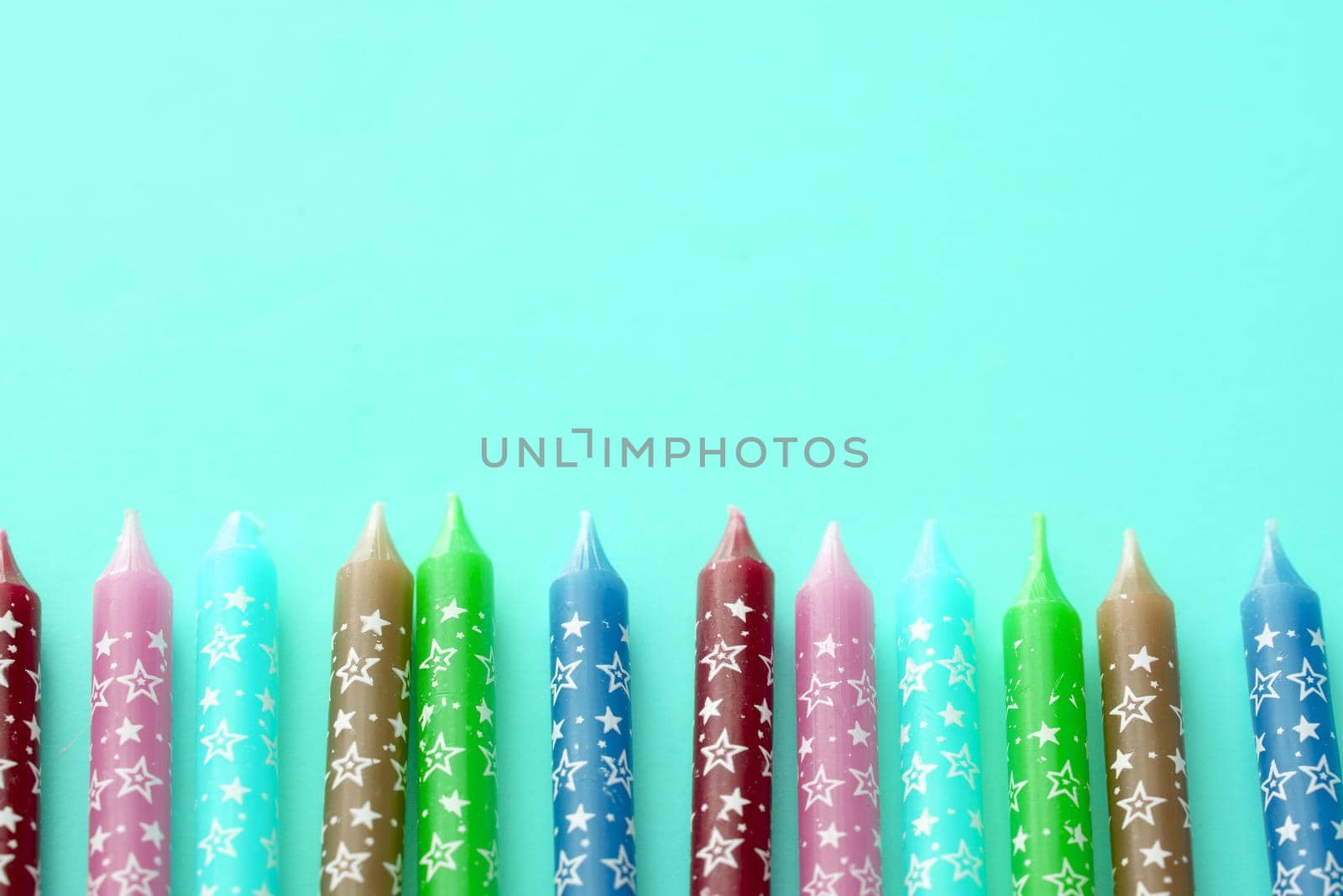 Row of birthday candles decorated with stars and colored green, maroon, blue, lavender against an aqua background