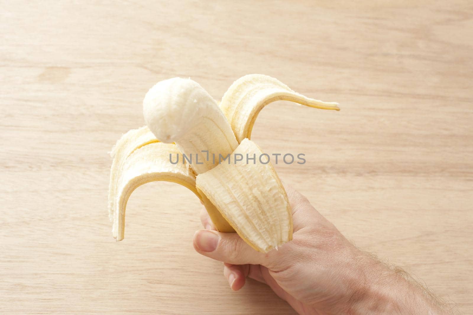 a hand holding a peeled half eaten banana with wood background