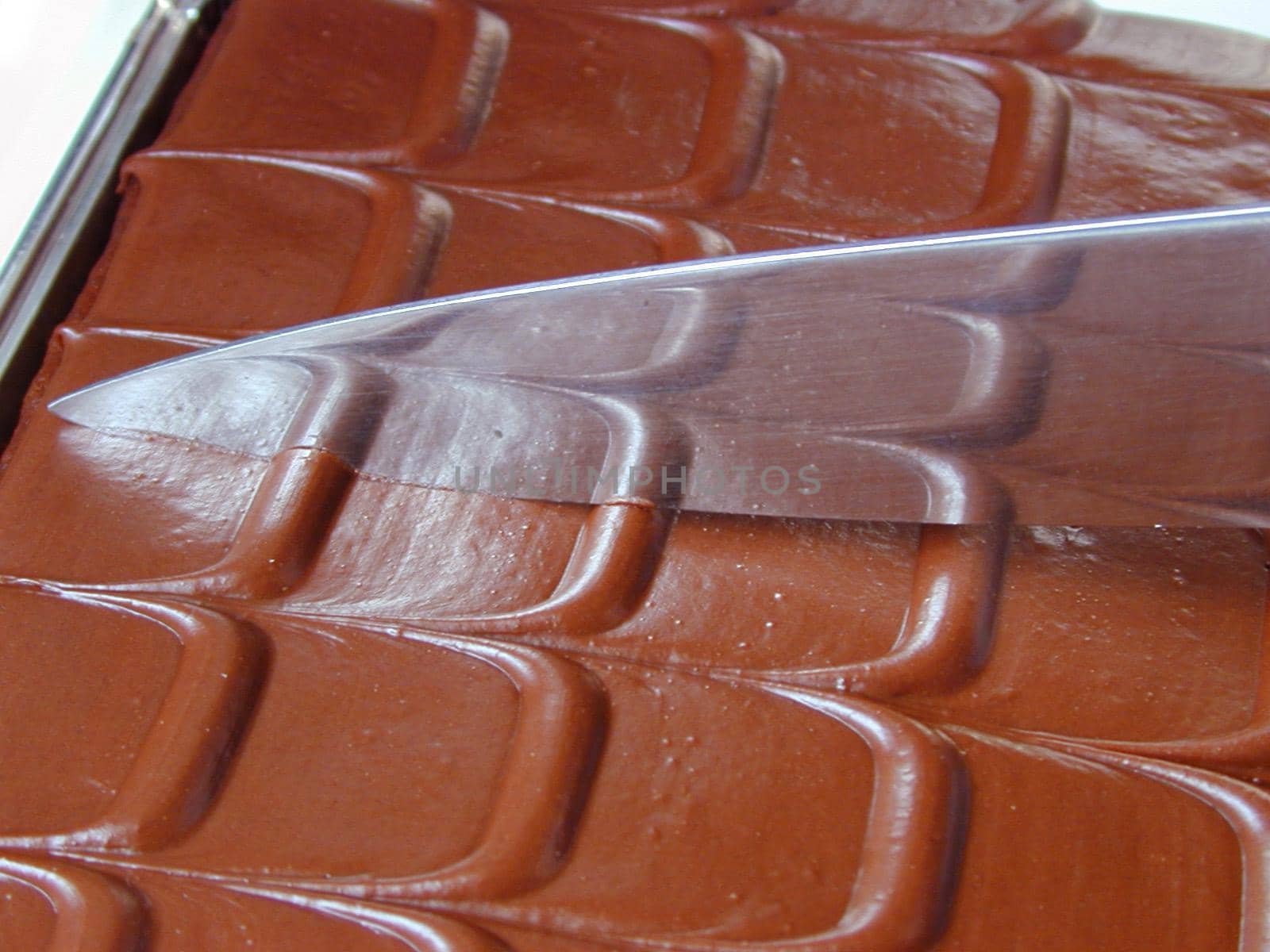 Cutting a delicious chocolate cake with a close up view of the blade of a knife resting on patterned chocolate icing