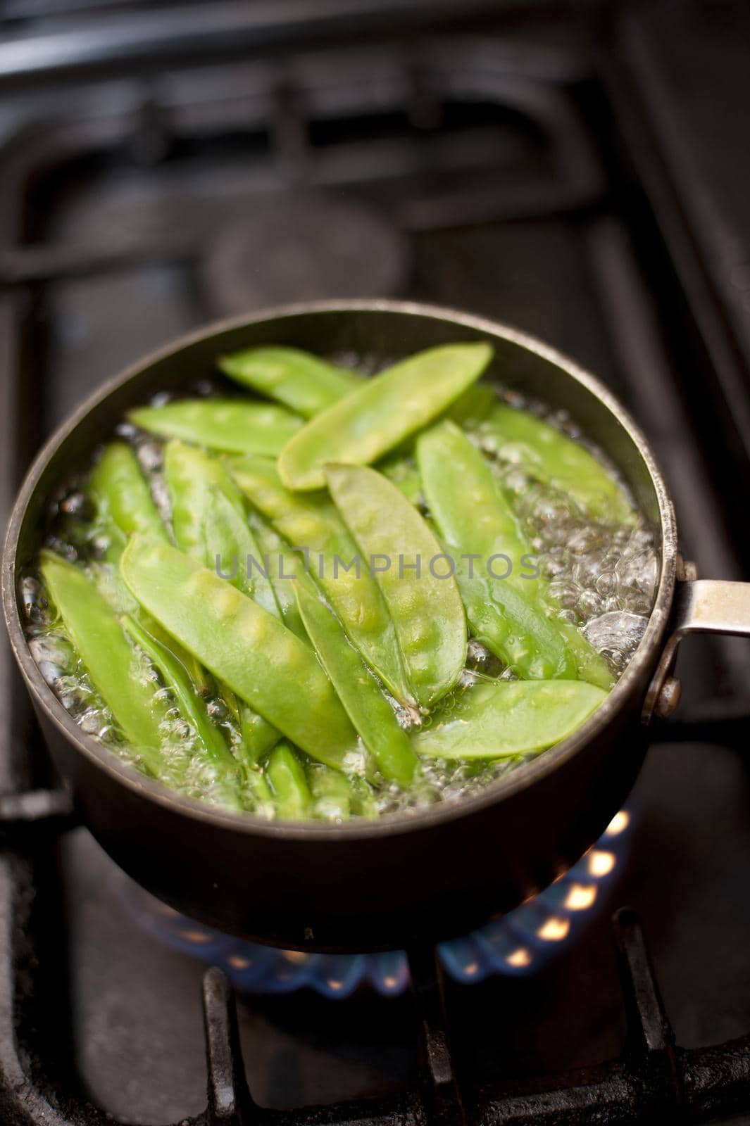 Cooking mangetout peas in a pot of boiling water on a gas hob, high angle view