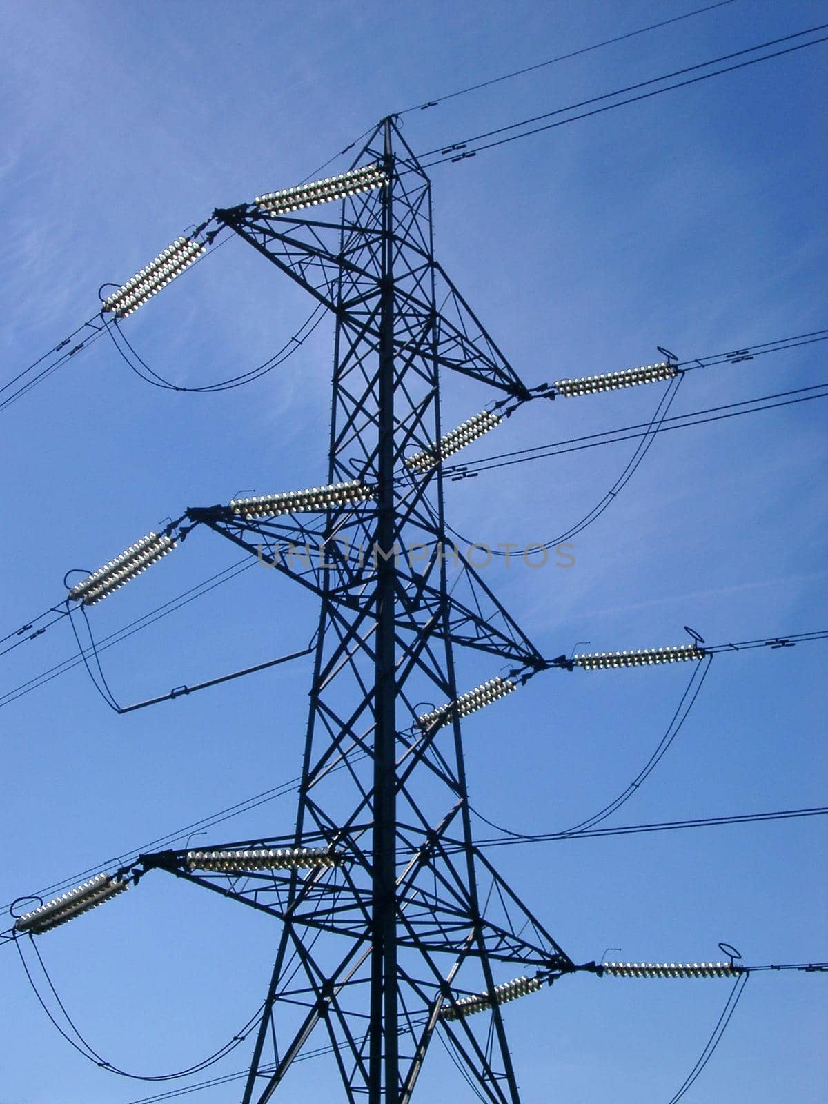 Detail of the top of an electricity pylon, showing all the connecting cables, against a clear blue sky