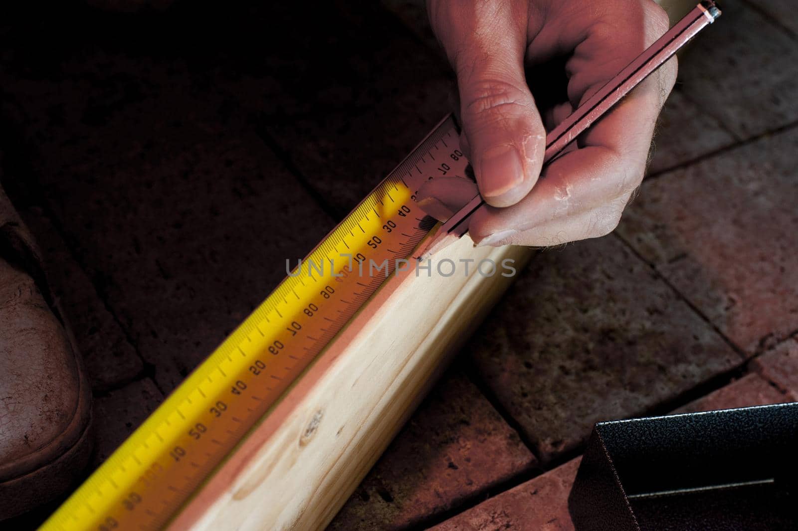 Carpenter carefully measuring a length of wood with a tape measure repeating his measurement a second time for accuracy
