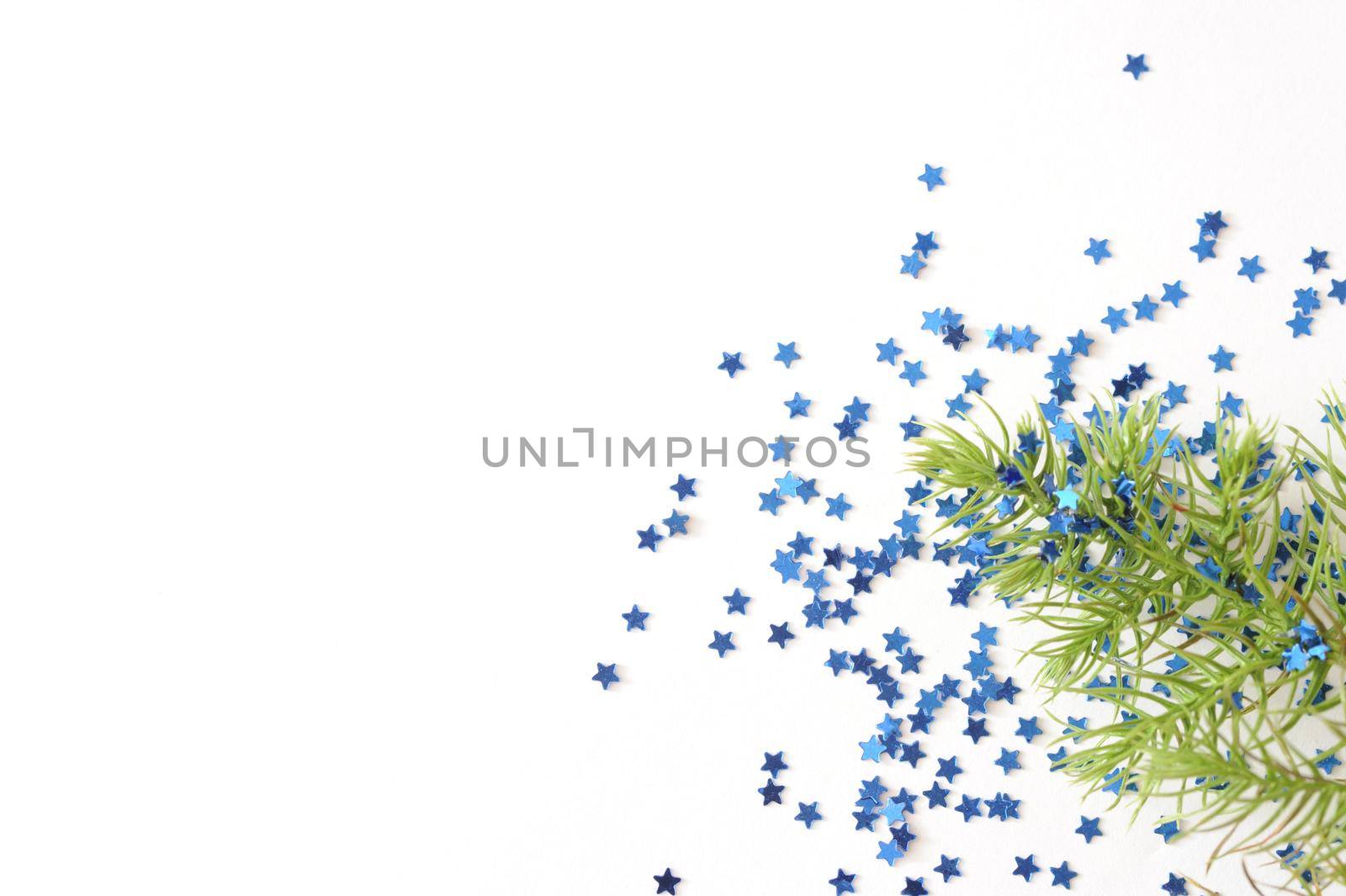 Sprig of Evergreen Tree Branch on White Background with Blue Star Shaped Glitter Confetti, Christmas Themed Image with Copyspace for Text
