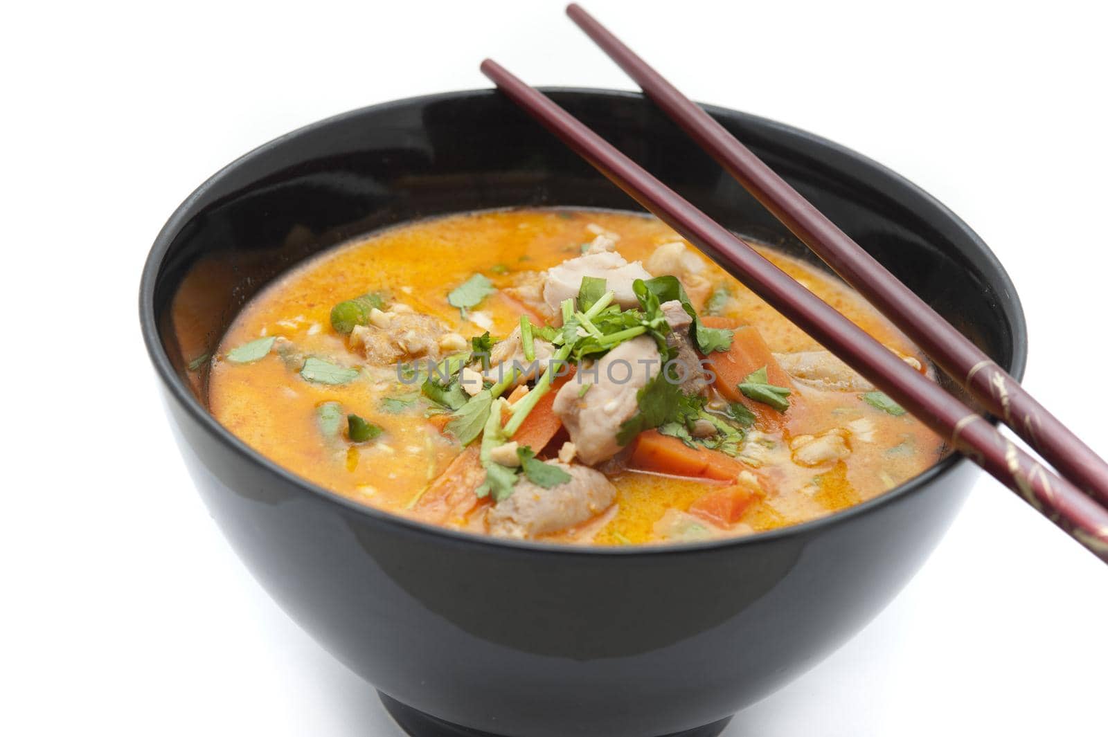 Delicious bowl of chicken laksa soup with vegetables and topped by cut herbs with chopsticks against a white background