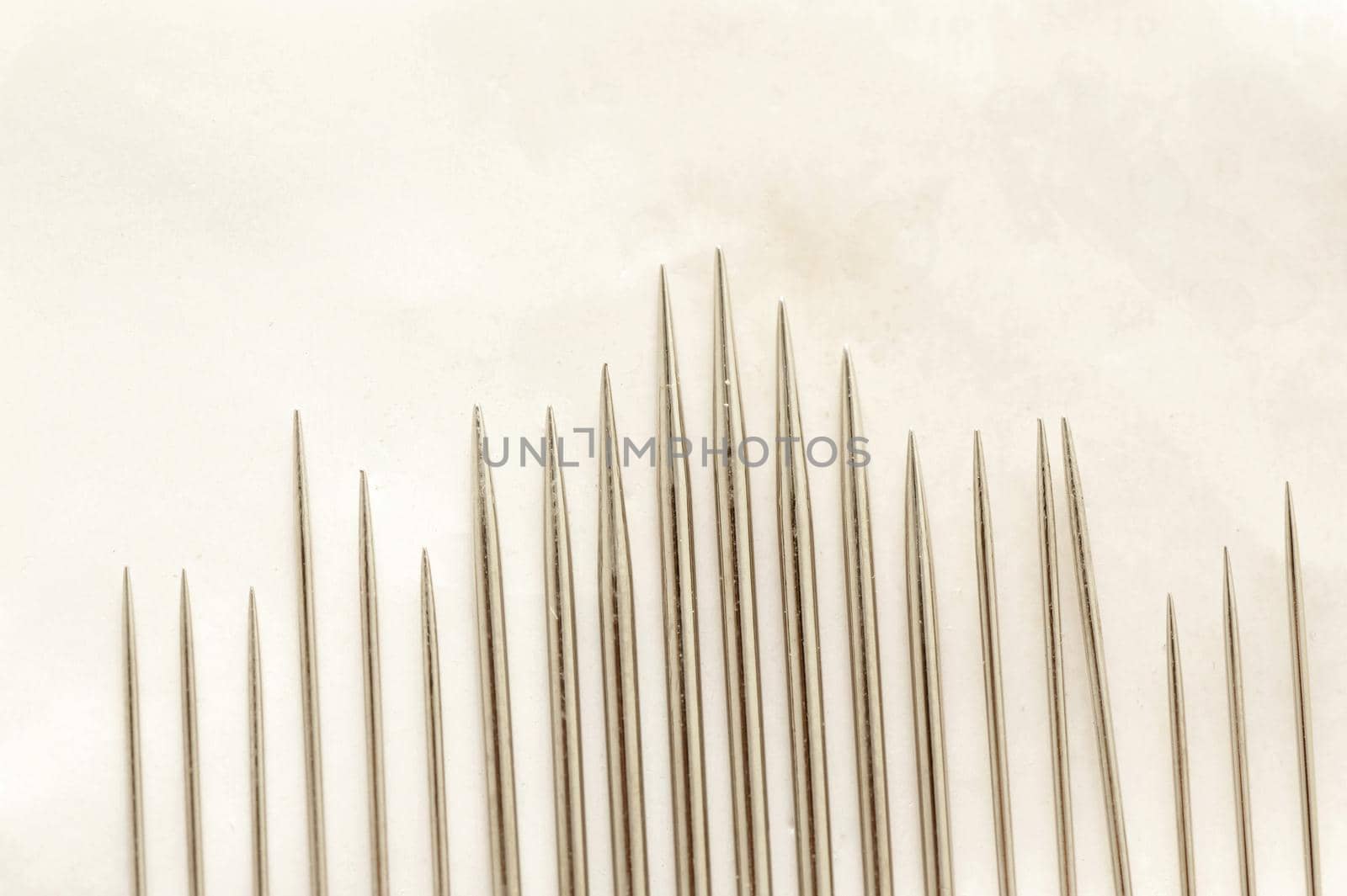 Close up on set of various sized sewing needle points organized by height and thickness over paper
