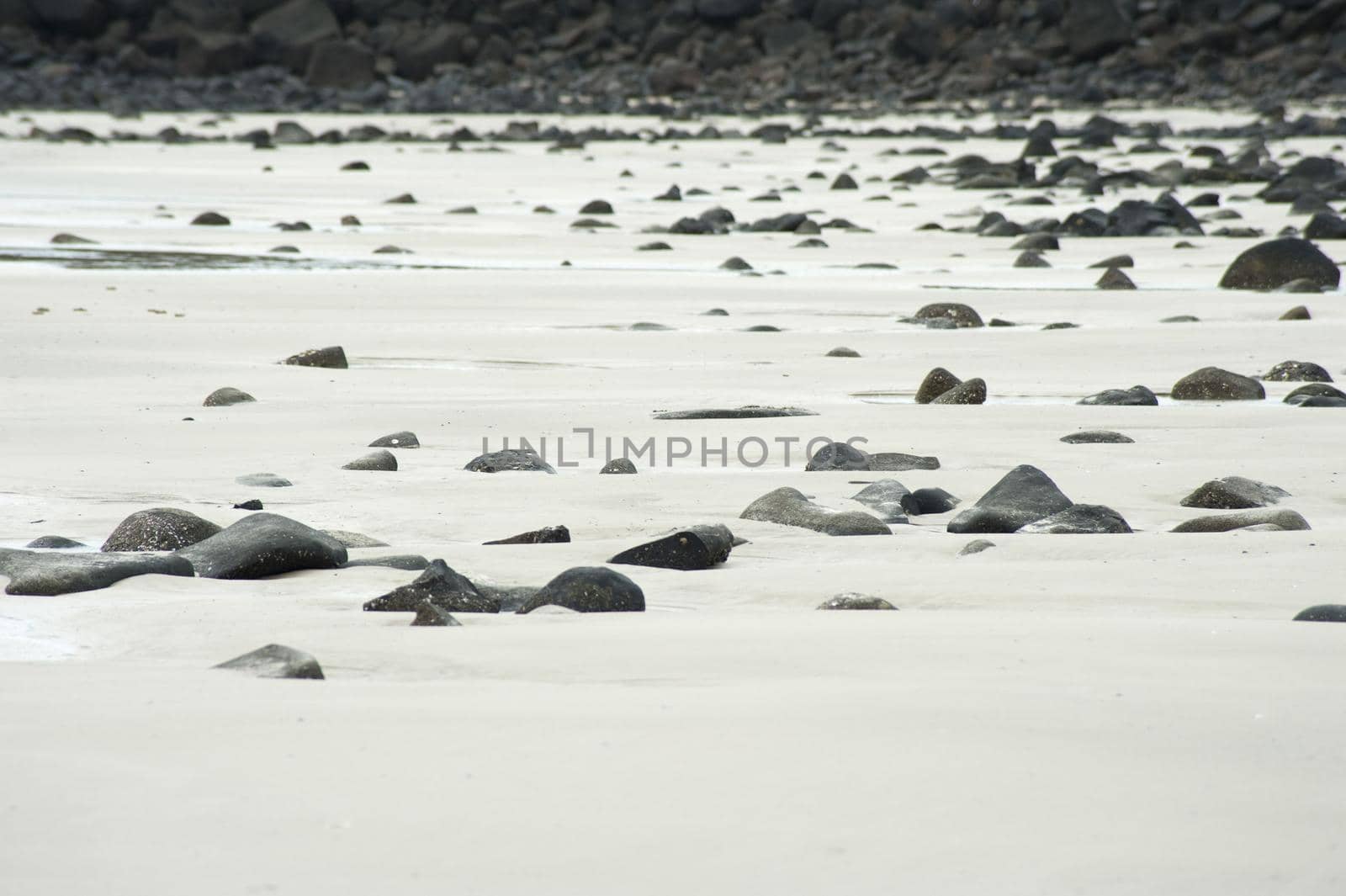 Plenty of Small to Medium Rocks at the Empty Seaside with White Sand.